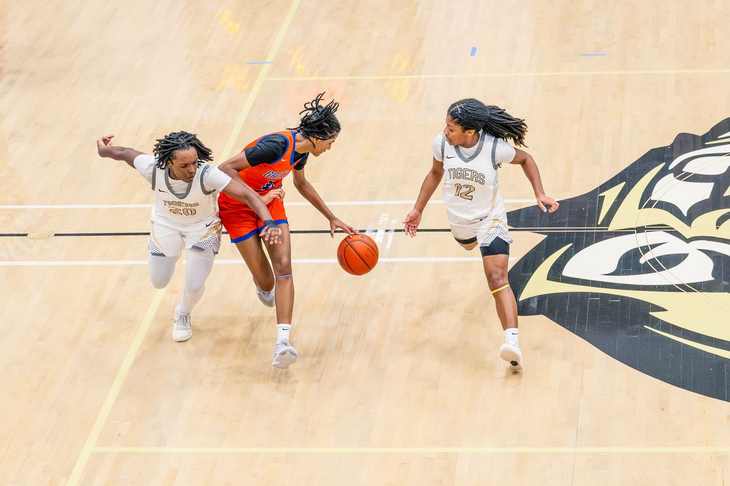 Three female basketball players battle for the ball during a competitive high school basketball game.