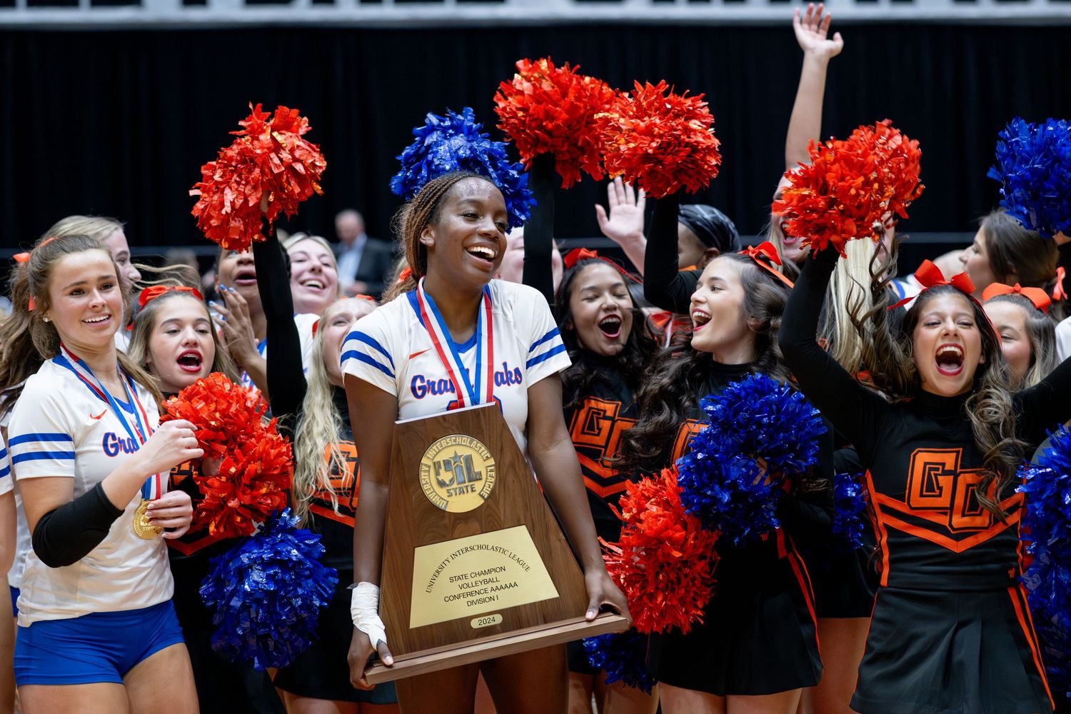 A student athlete holds a UIL championship trophy surrounded by cheerleaders.