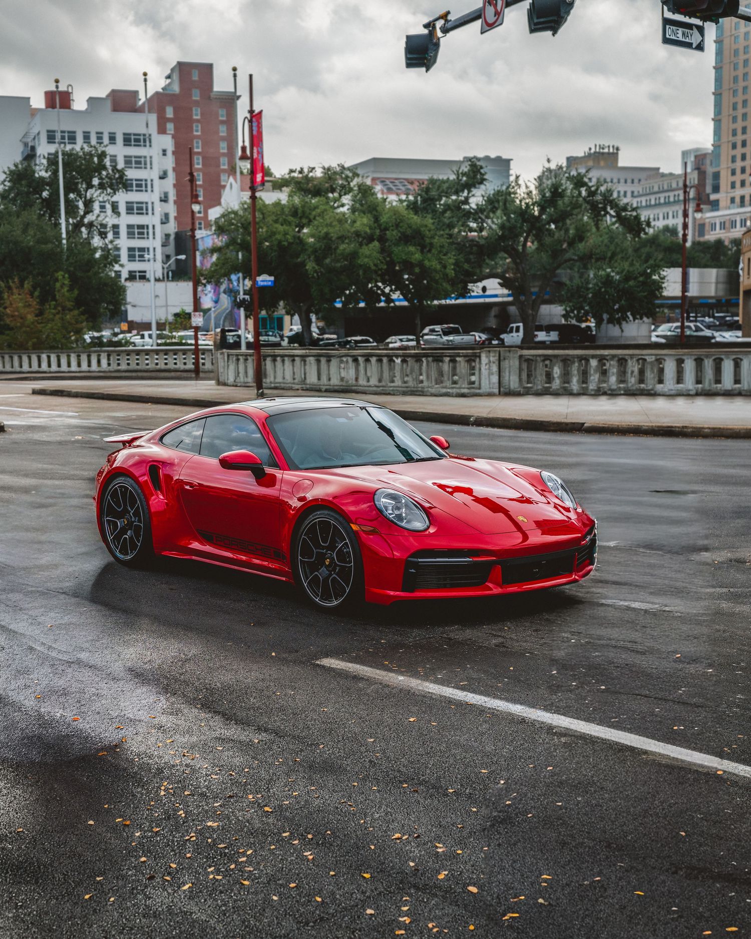 Red Porsche 911 Turbo S driving through a wet city intersection on an overcast rainy day.