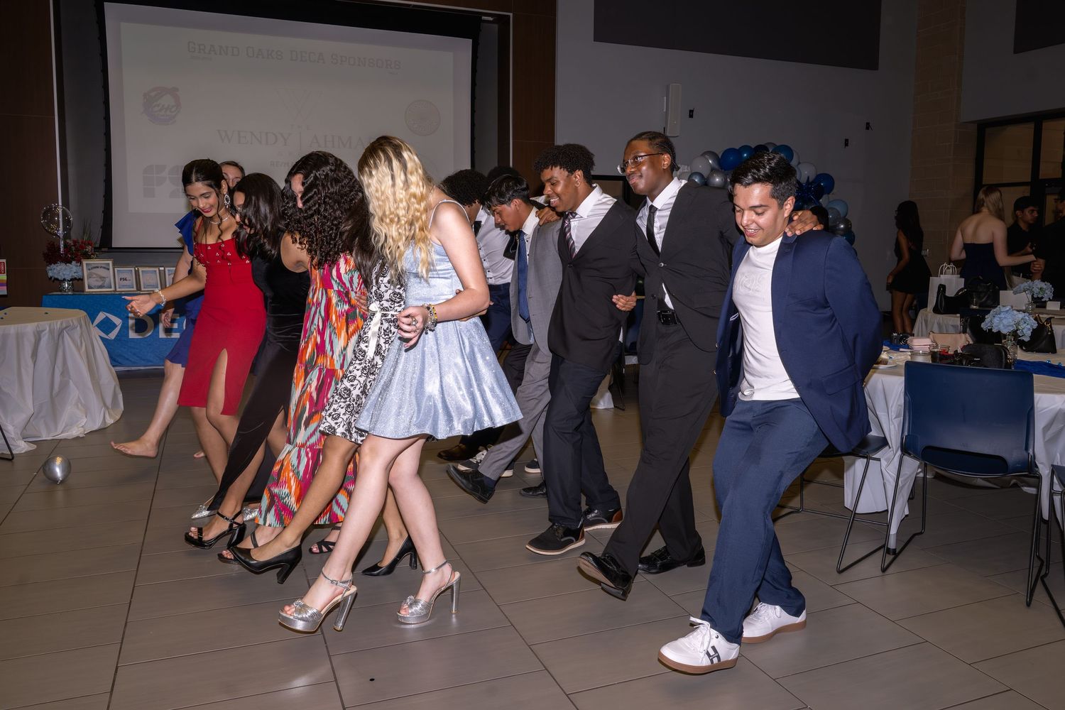 Teens dancing in formal attire at a school banquet event in a decorated hall.