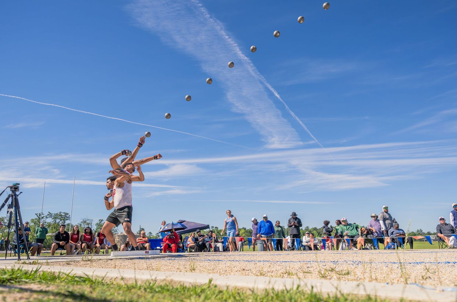 Athlete throwing shot put with multiple exposure effect showing the arc of the throw outdoors.