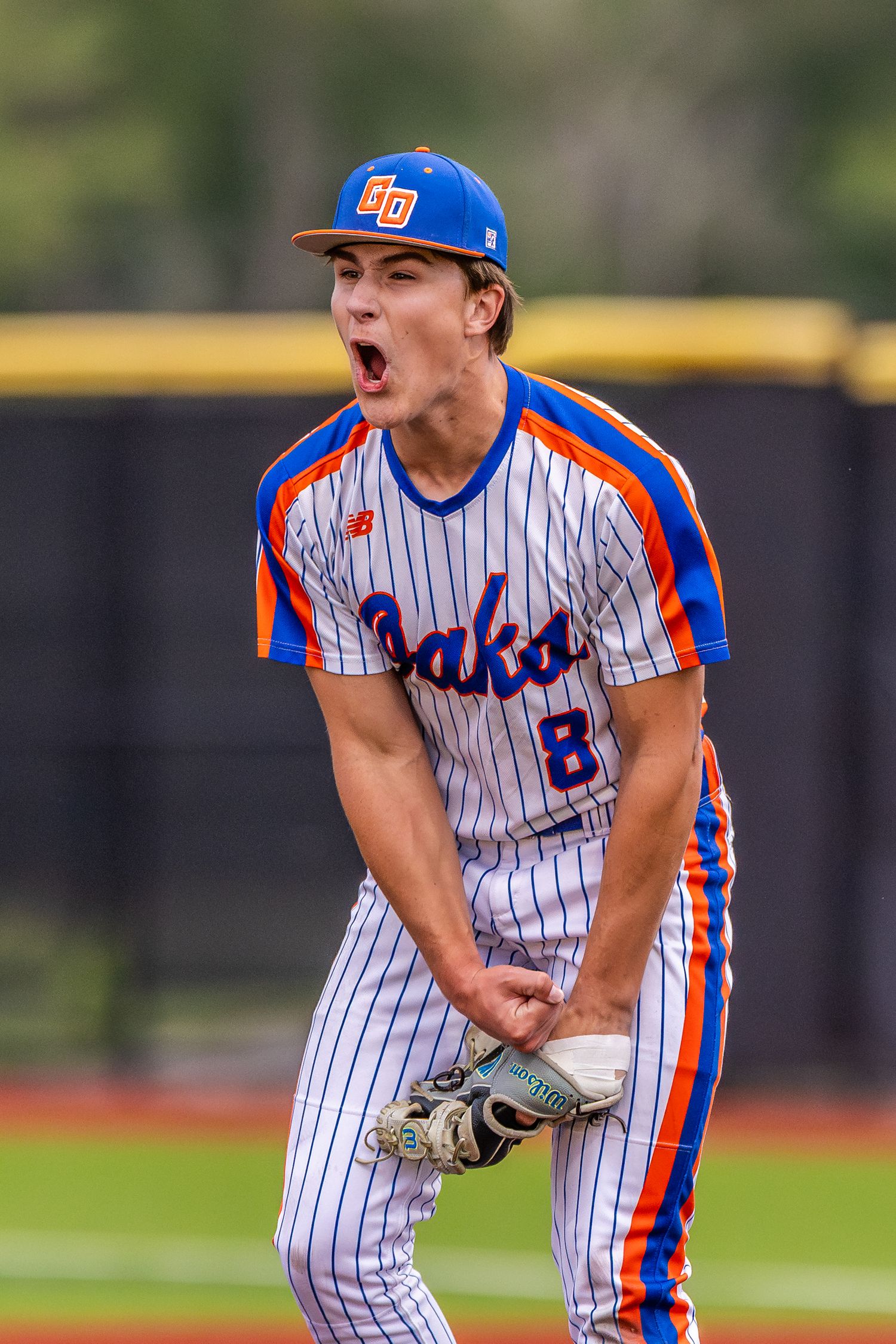 Oaks baseball pitcher celebrates intensely in blue and orange pinstripe uniform.