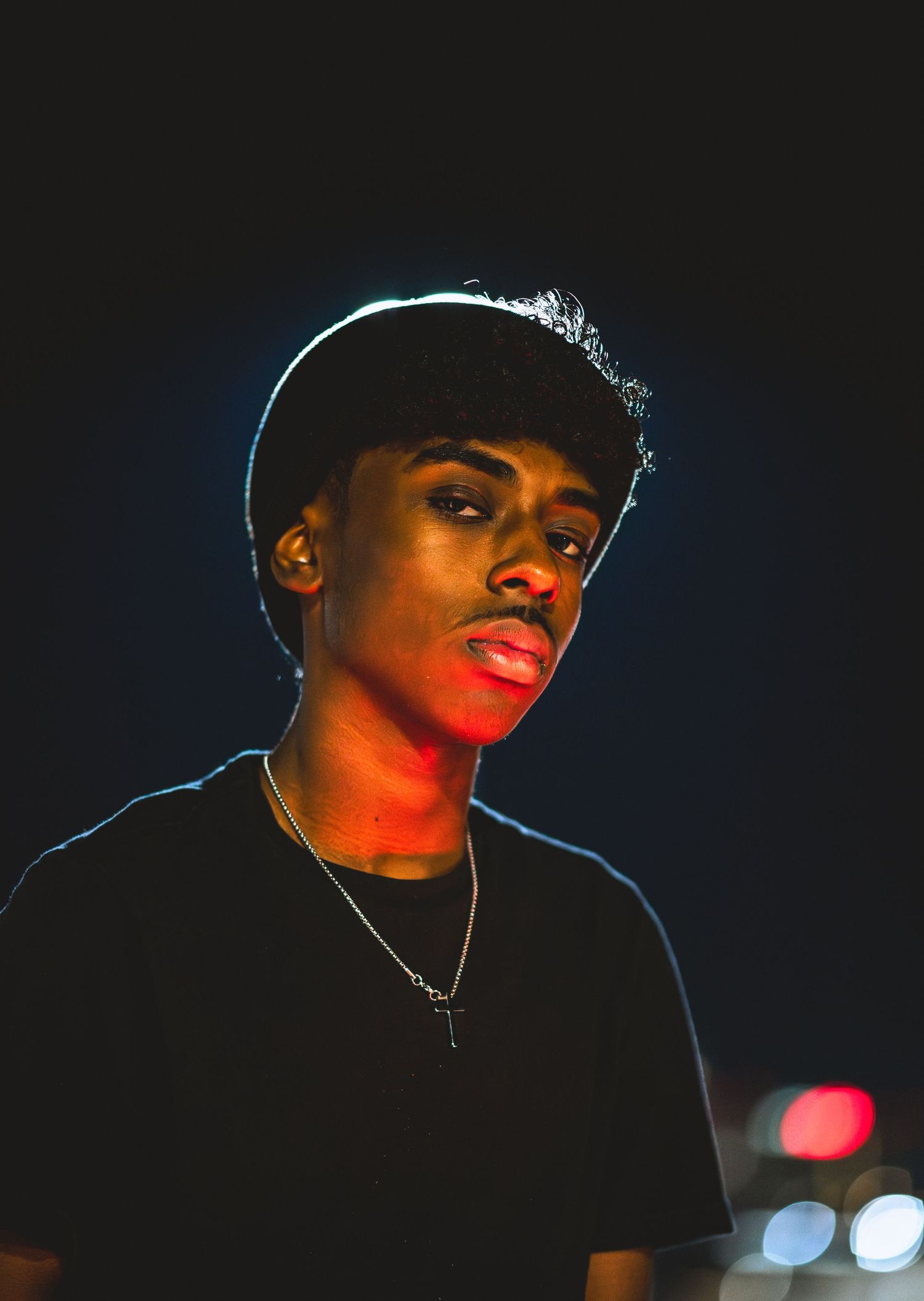 Close-up portrait of young man with chain necklace illuminated by red light at night.