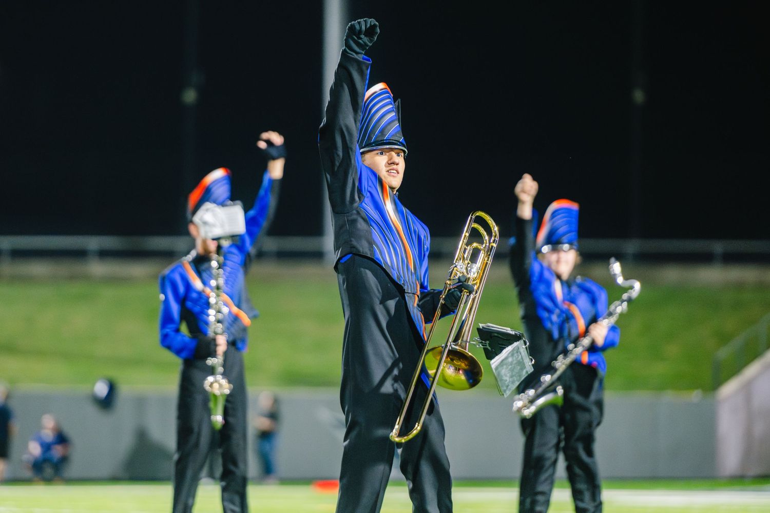 Marching band trombone player raises fist triumphantly during a nighttime halftime field performance.