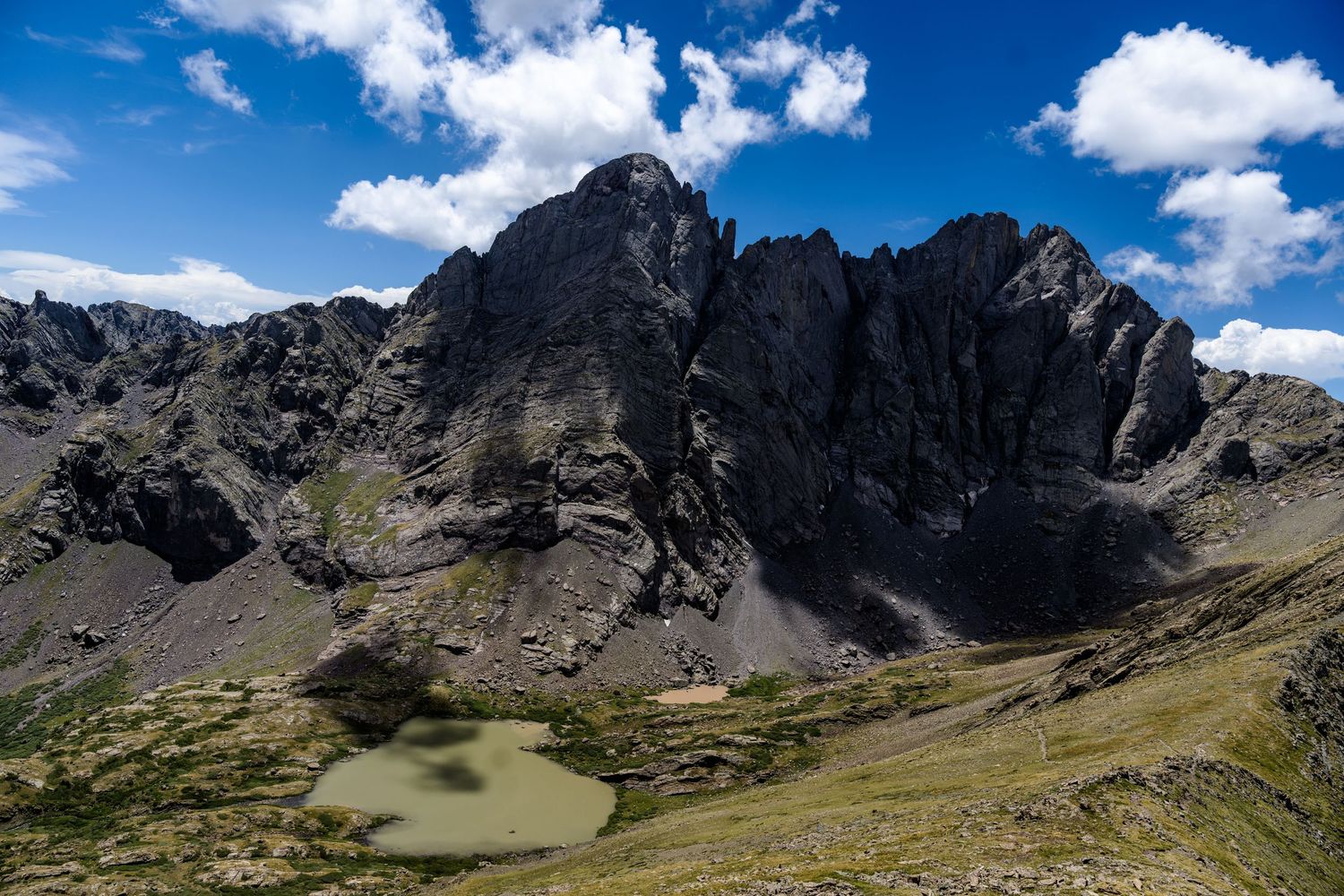 Aerial view of jagged mountain peaks with a small alpine lake nestled in a rocky valley.
