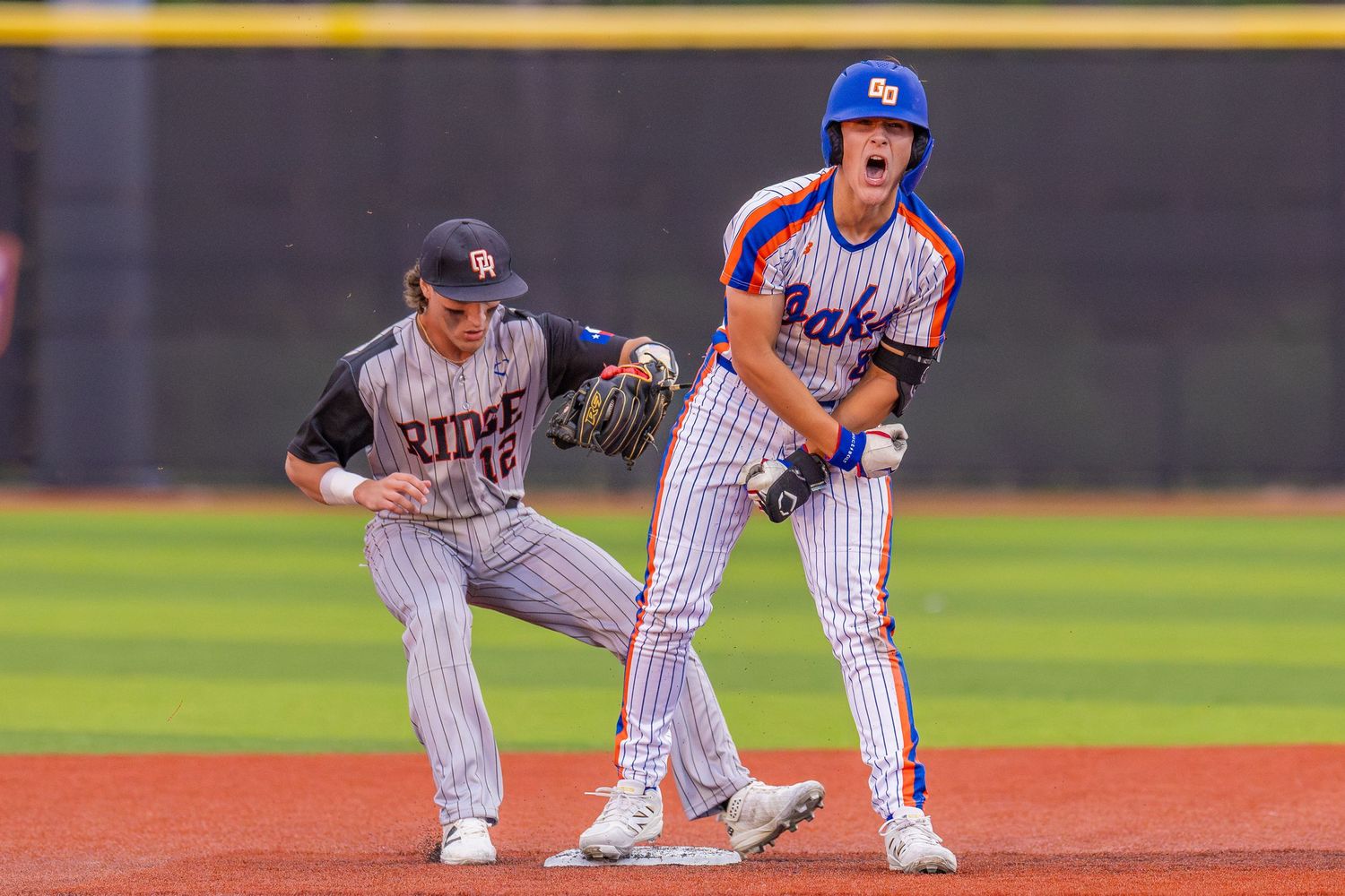 Two baseball players compete at second base during a high school game in blue uniforms.