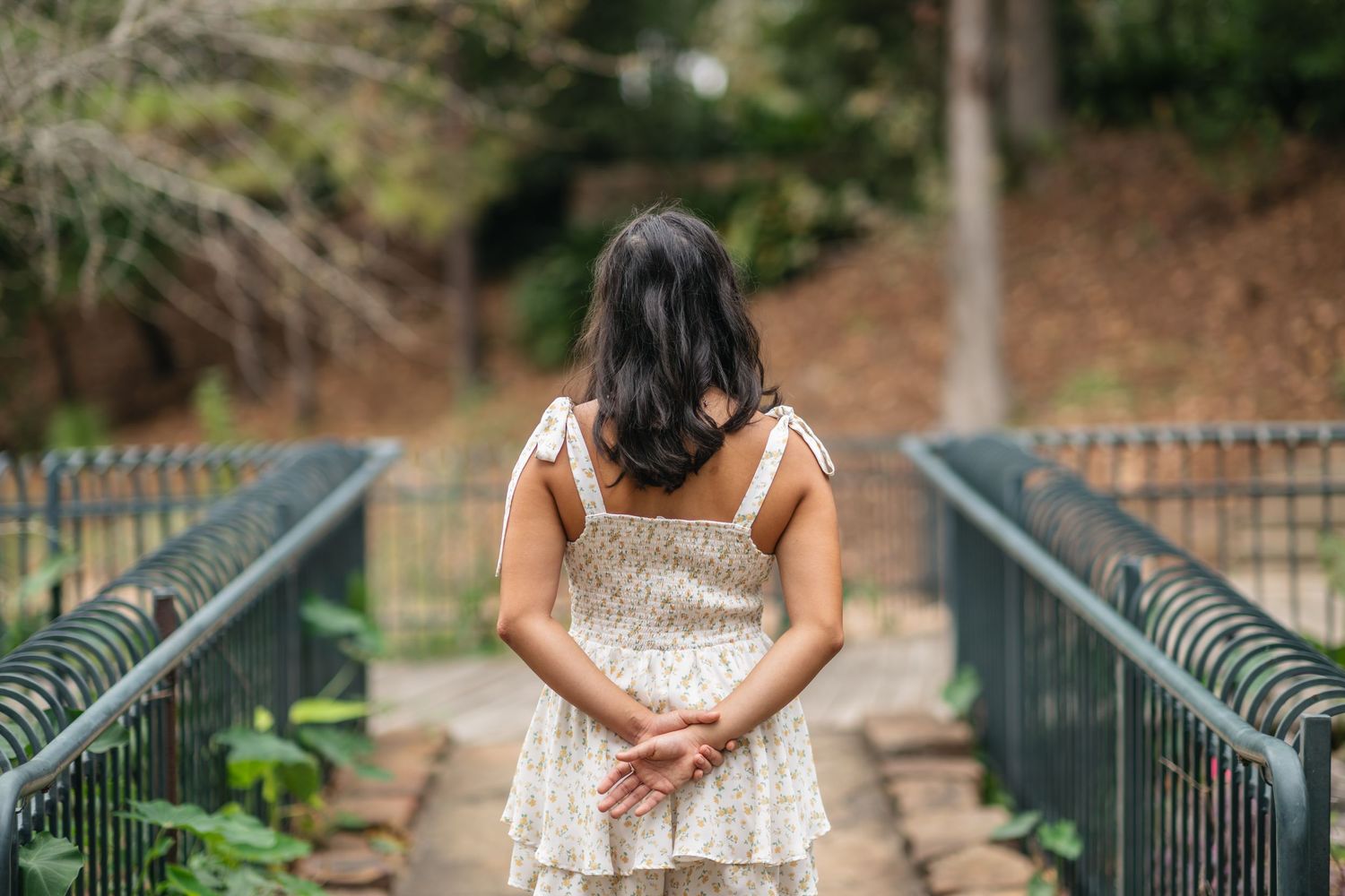 A senior portrait of a young woman standing on a bridge path from behind.