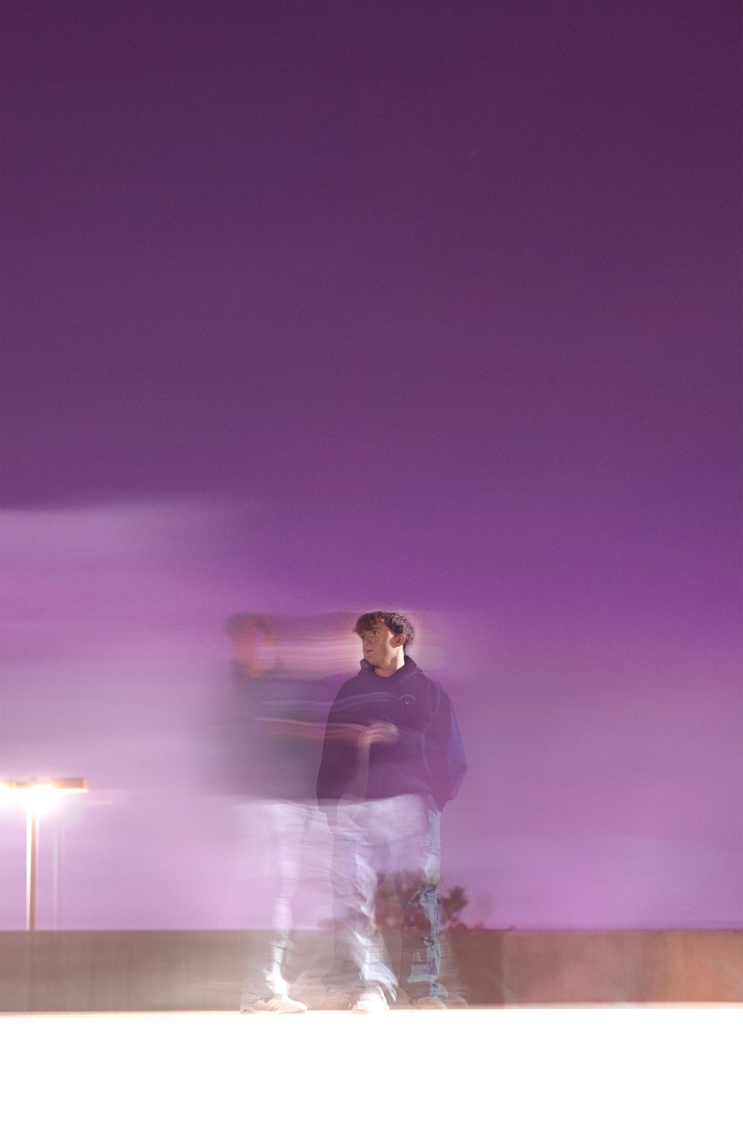 A long exposure photo of a man in a purple hoodie against a vivid purple night sky creating a ghostly motion blur.