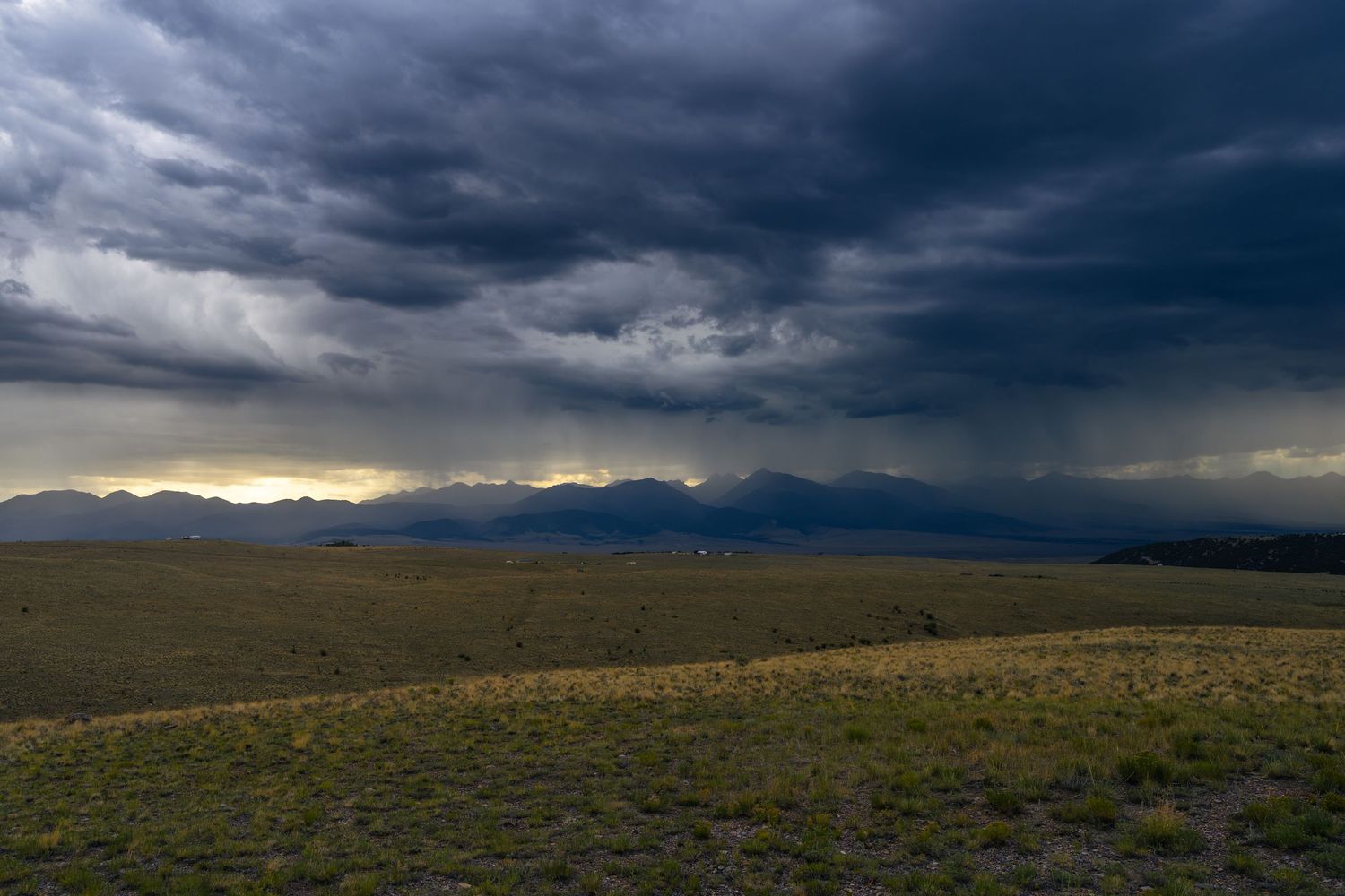 Dark storm clouds rolling over a vast flat plain with distant mountains at sunset.