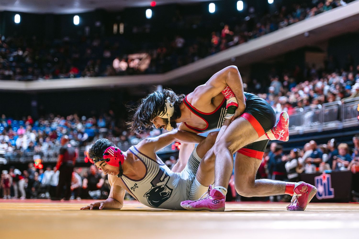 Two wrestlers compete intensely on the mat in front of a packed arena audience during a championship match.