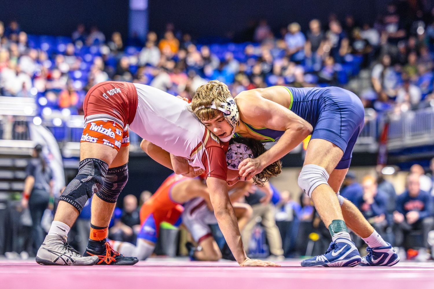 Two wrestlers compete intensely on pink mat at state championship wrestling tournament.