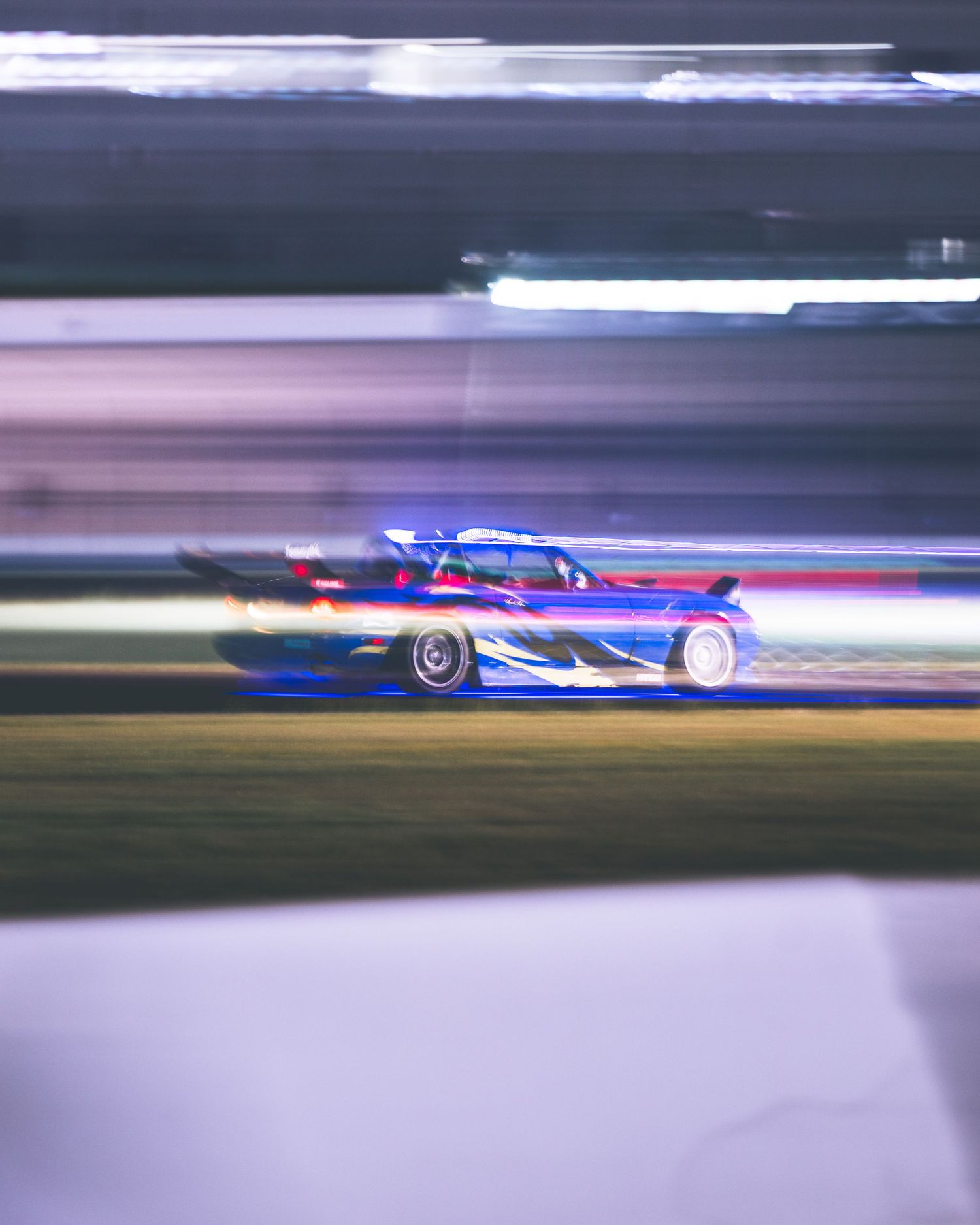 A drift car with blue and red livery captured with motion blur racing on a track at night.
