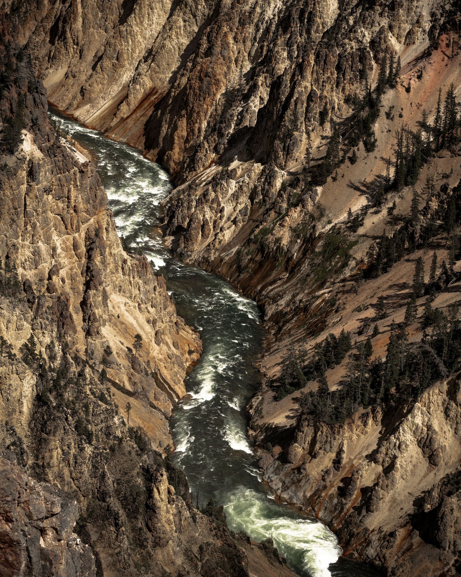 Aerial view of a rushing river winding through the rugged Grand Canyon of Yellowstone with steep rocky cliffs.