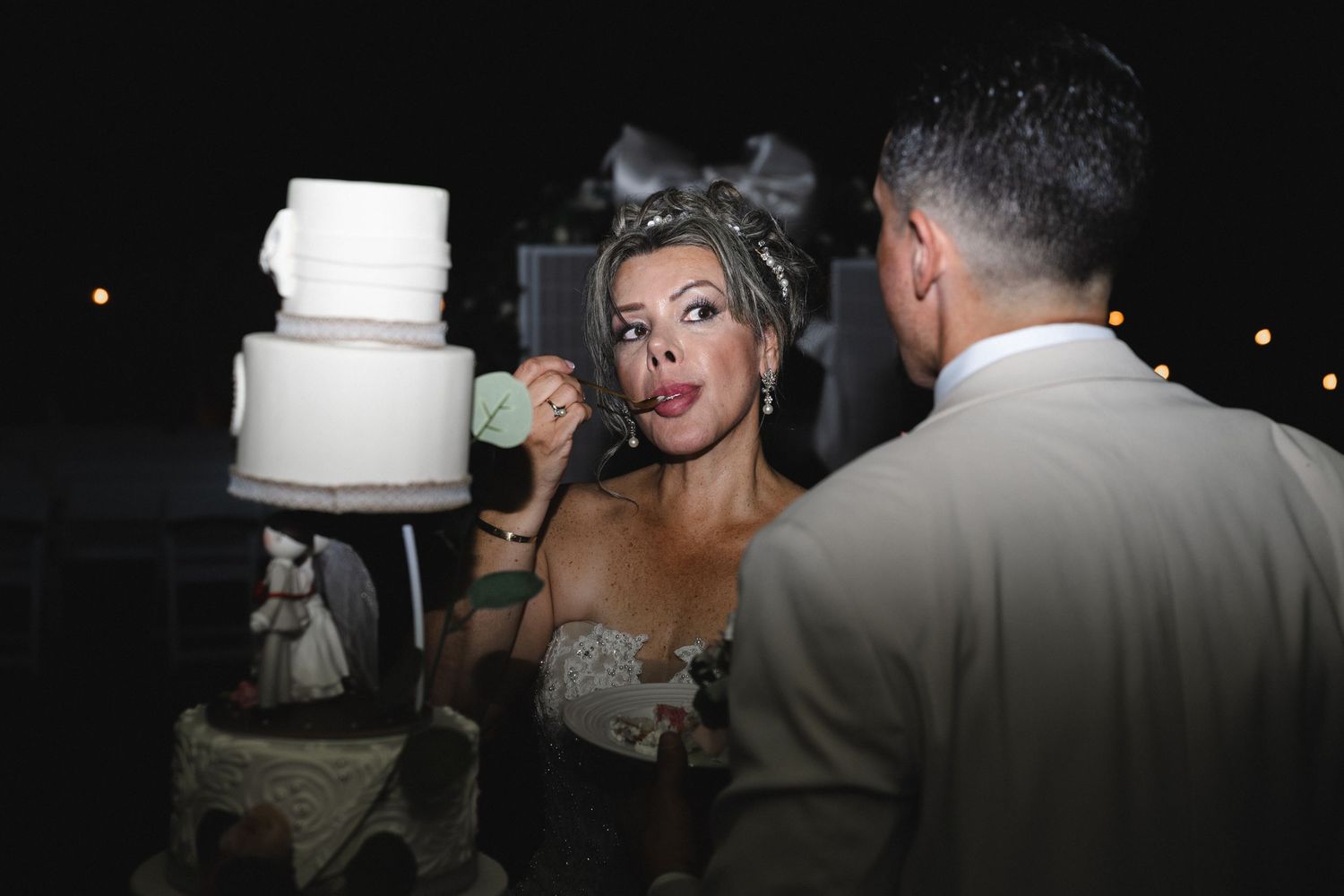 Bride and groom cutting their elegant white tiered wedding cake at a nighttime outdoor reception celebration.