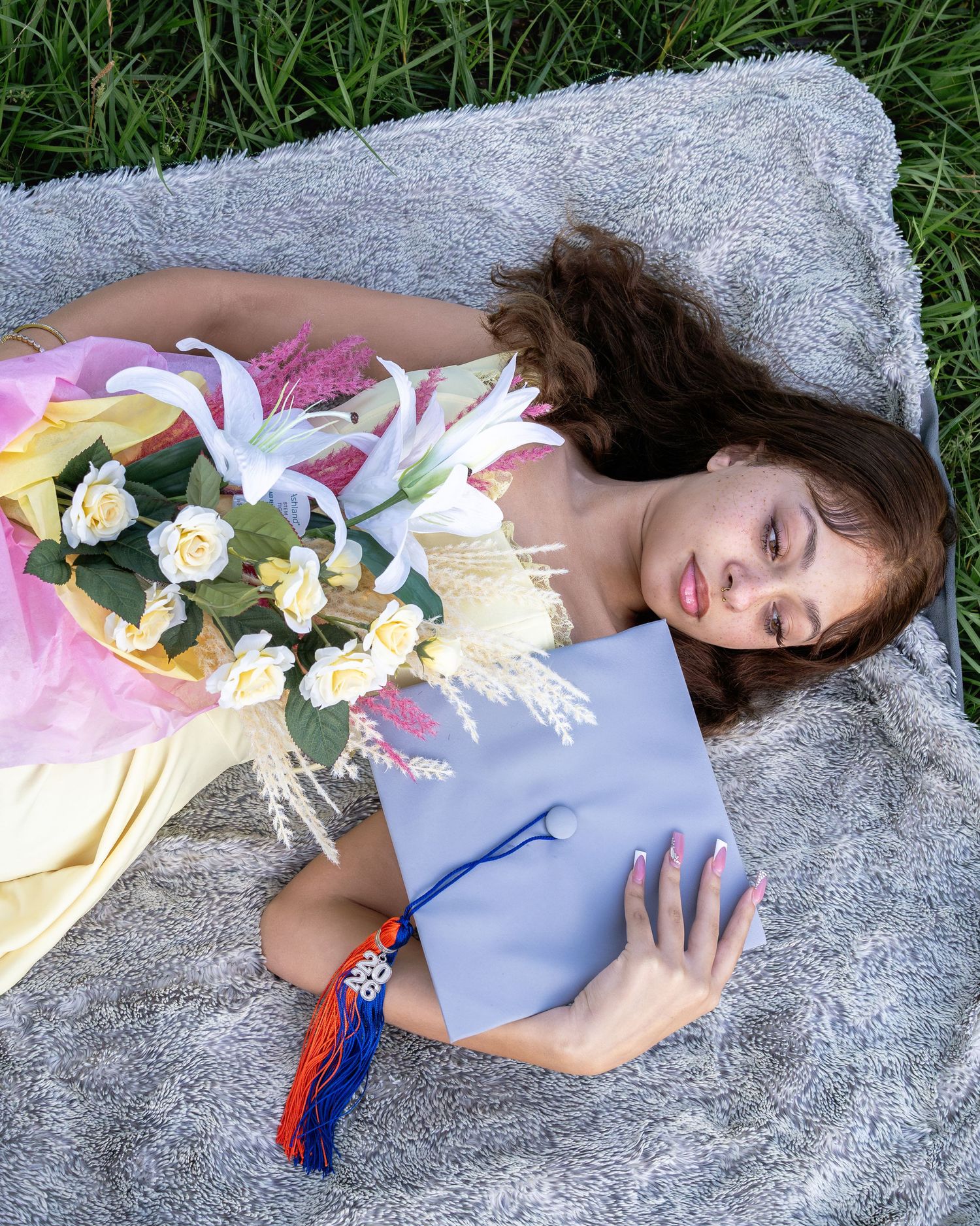 Graduate lying on blanket holding cap and bouquet of white lilies for senior photos.