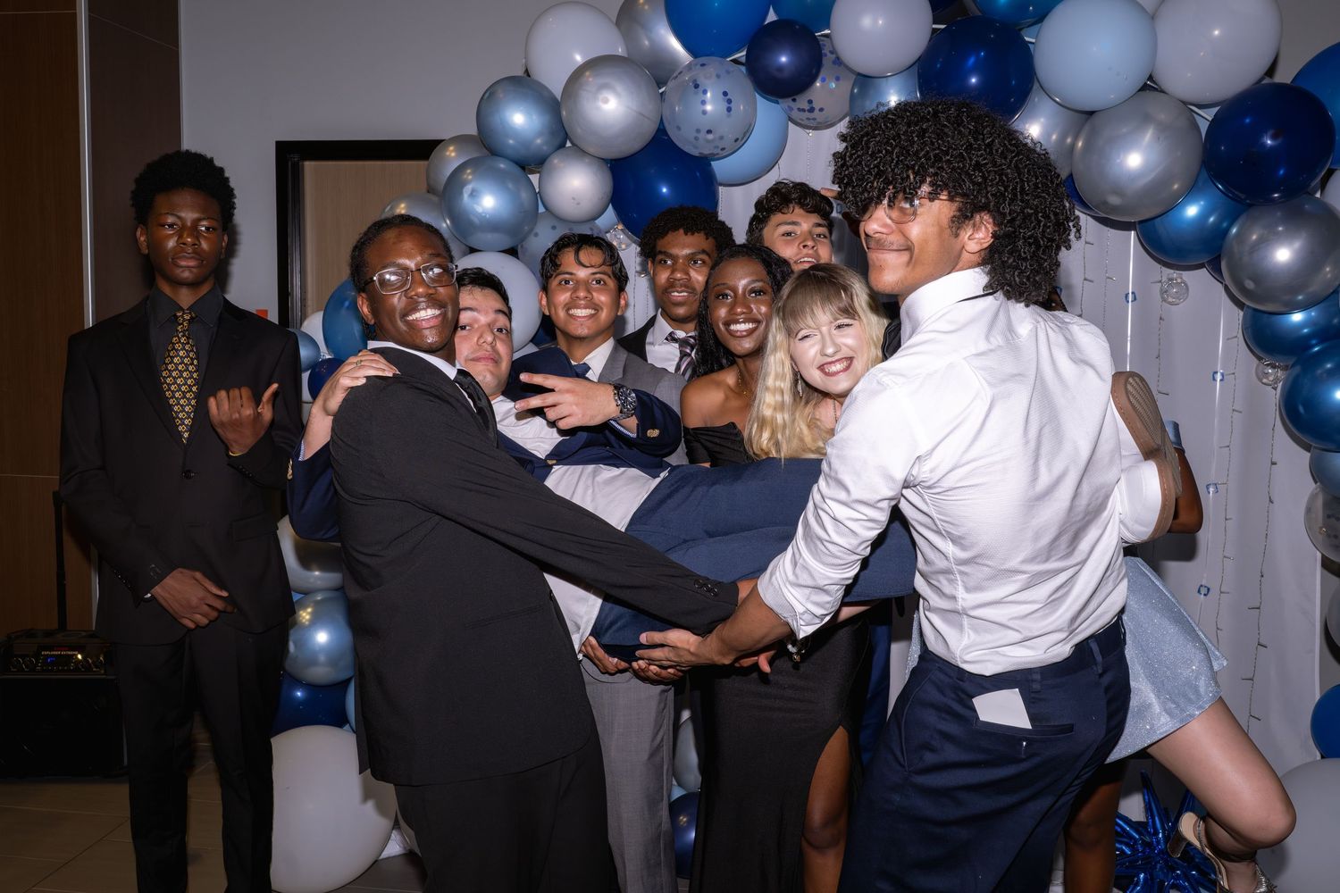 Teens in formal attire celebrate banquet night with balloons and playful poses at a blue and white themed event.
