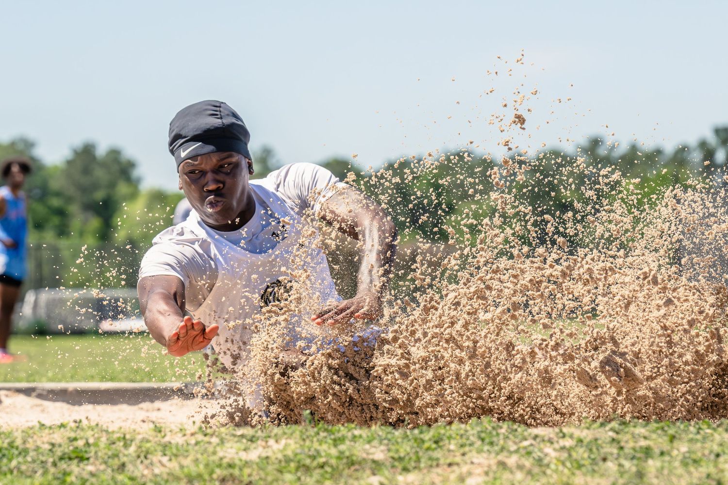 Athlete landing in a sand pit during a long jump competition on a sunny day.