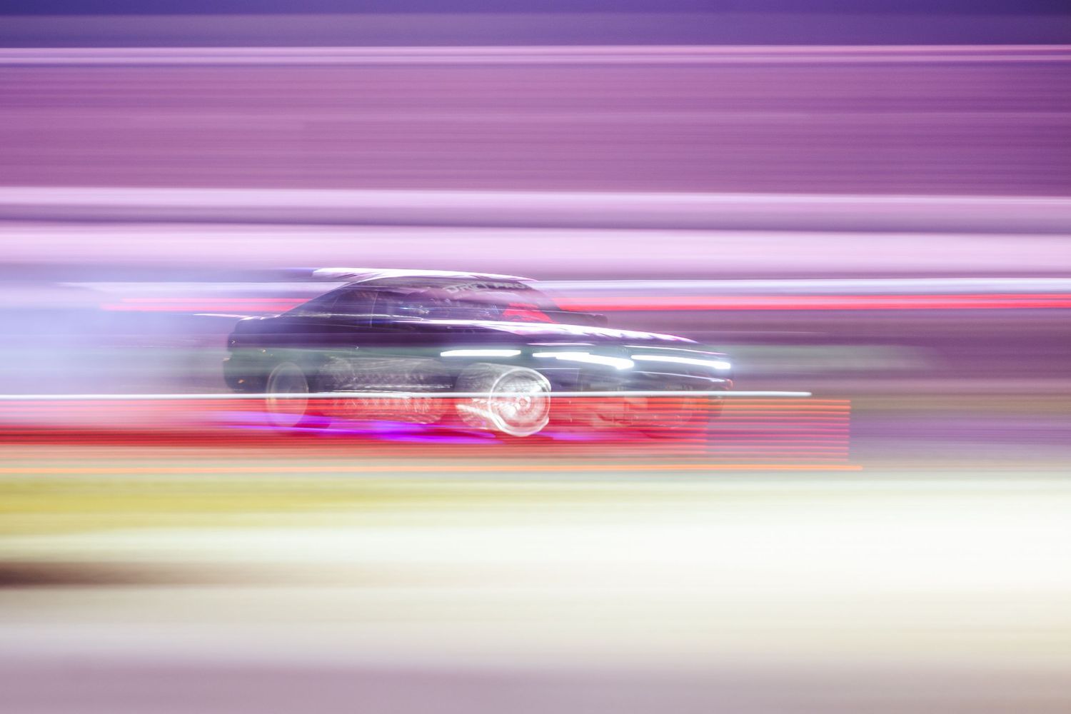 Motion blur photo of a racing car speeding past with colorful light streaks in pink and yellow tones.