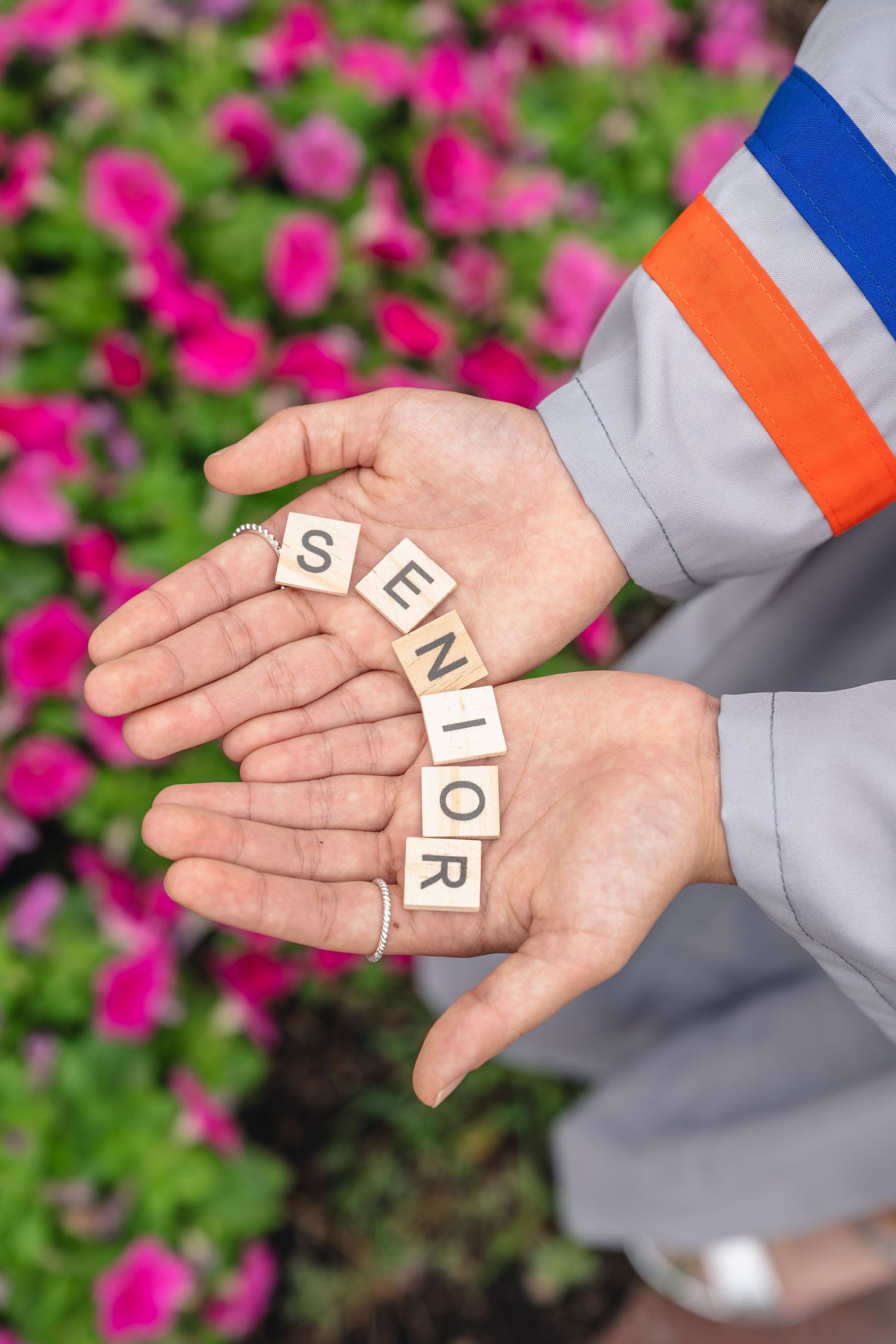 Hands holding Scrabble tiles spelling SENIOR in front of pink flowers.