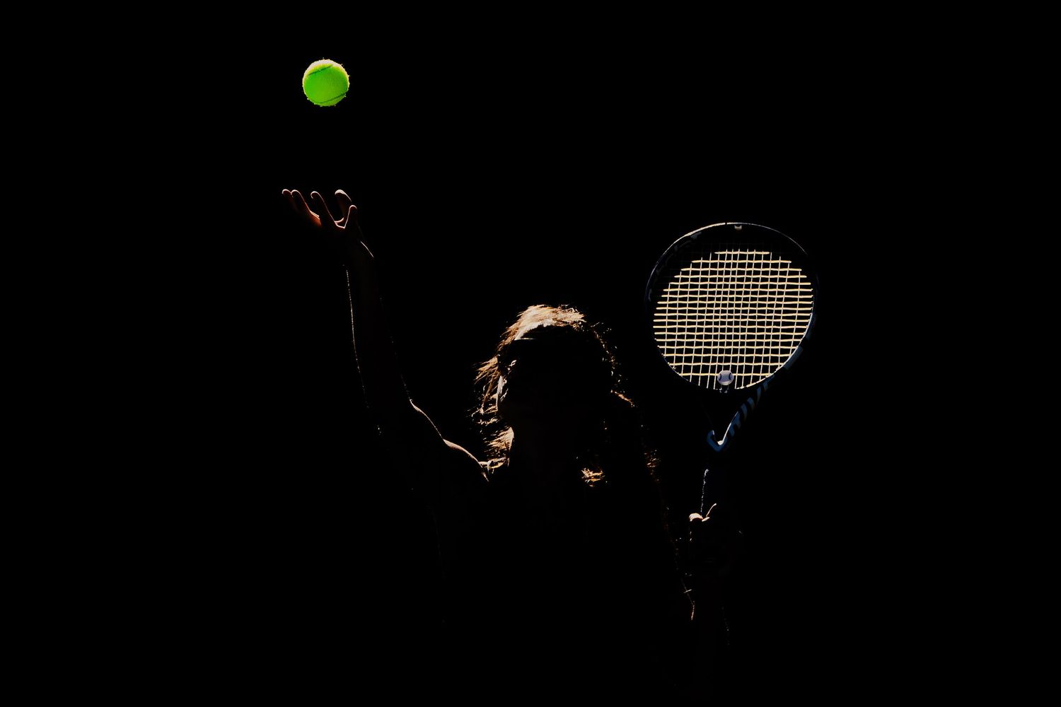 Silhouette of a tennis player serving a glowing green ball against a dark black background.