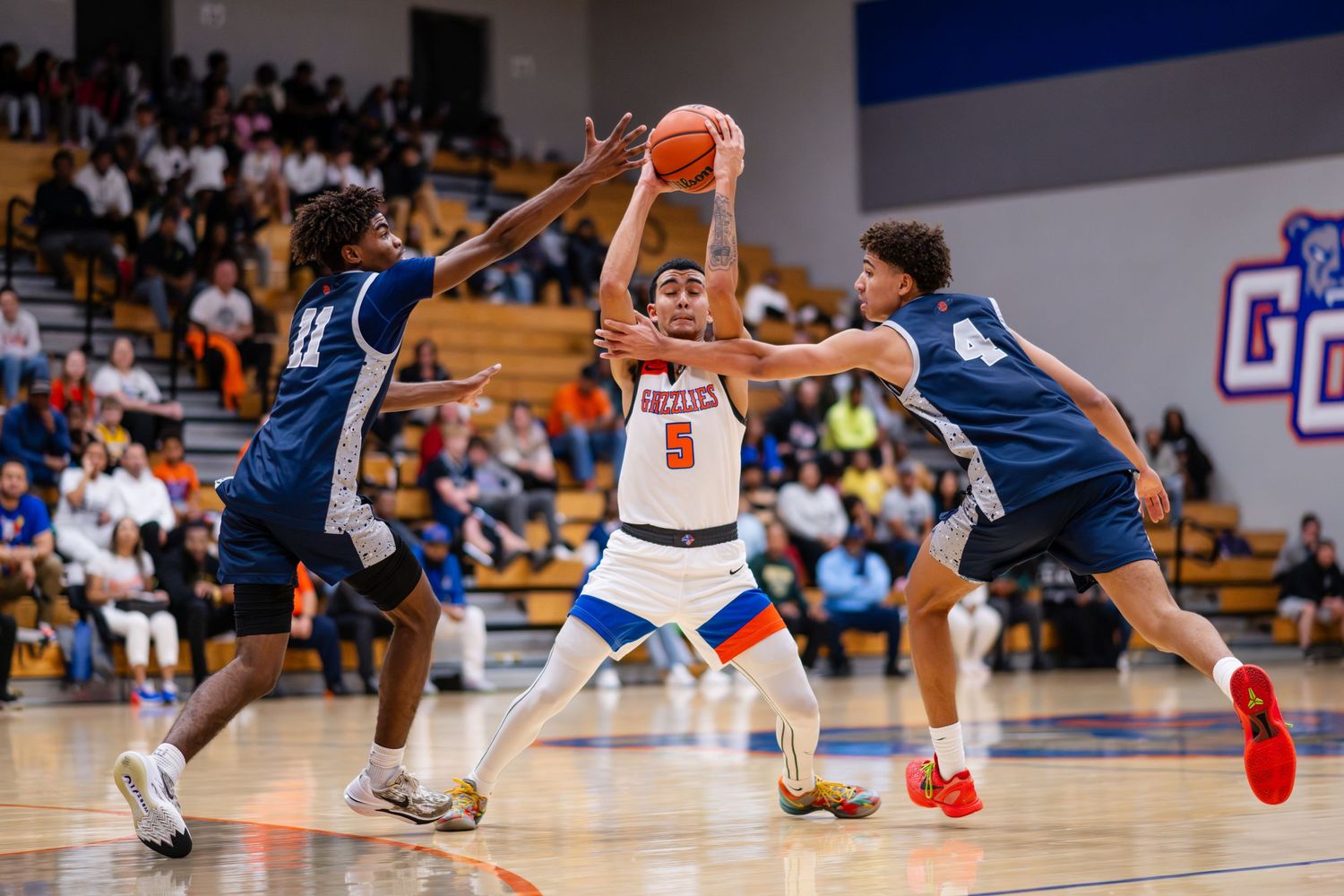 A basketball player drives to the hoop between two defenders during a high school game.