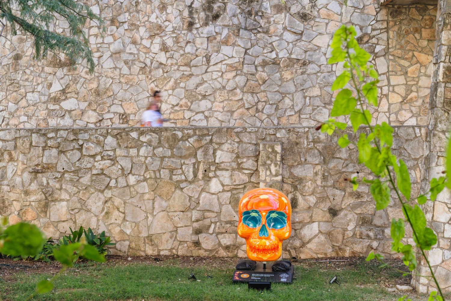 Colorful orange Day of the Dead sugar skull sculpture displayed against a rustic stone wall outdoors.