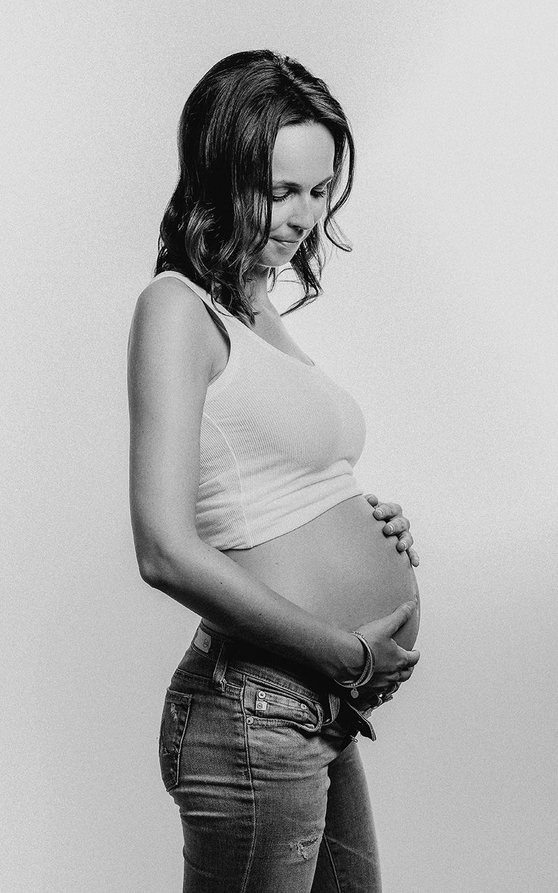 Schwangere Frau im Fotostudio vor heller Wand.