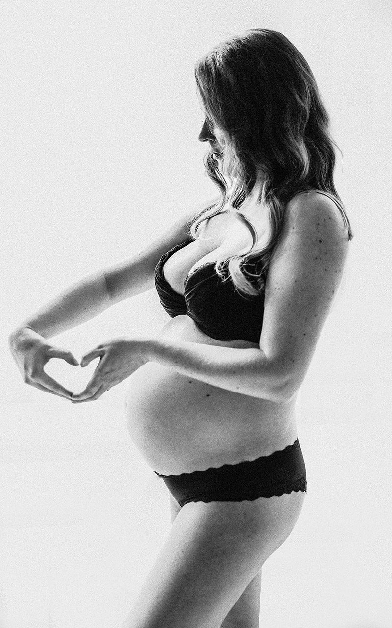 Silhouette einer schwangeren Frau im Fotostudio. Sie hat ihre finder zu einem Herz geformt.
