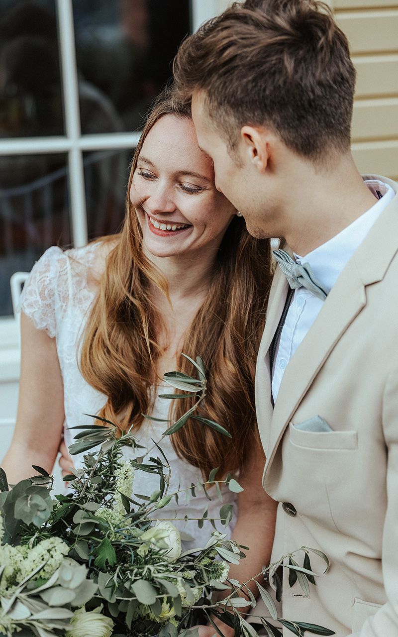 Brautpaar umarmt sich sitzend mit grossem Blumenstrauss in der Hand.