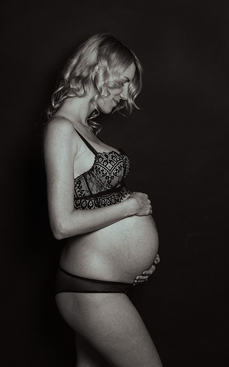 Schwangere Frau trägt schwarze spitzen Dessous und steht im Fotostudio.