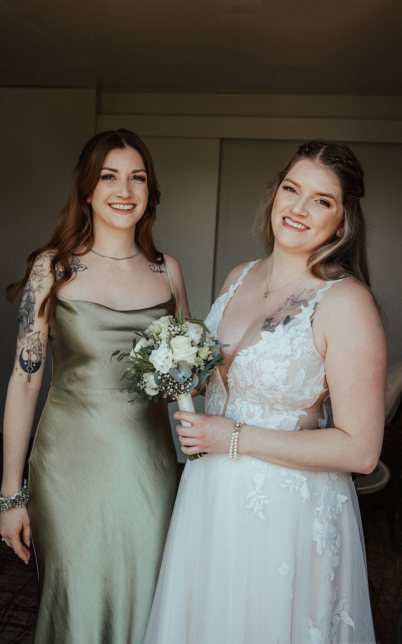 Braut mit Schwester in schönen Kleidern und Blumenstrauß in der Hand.