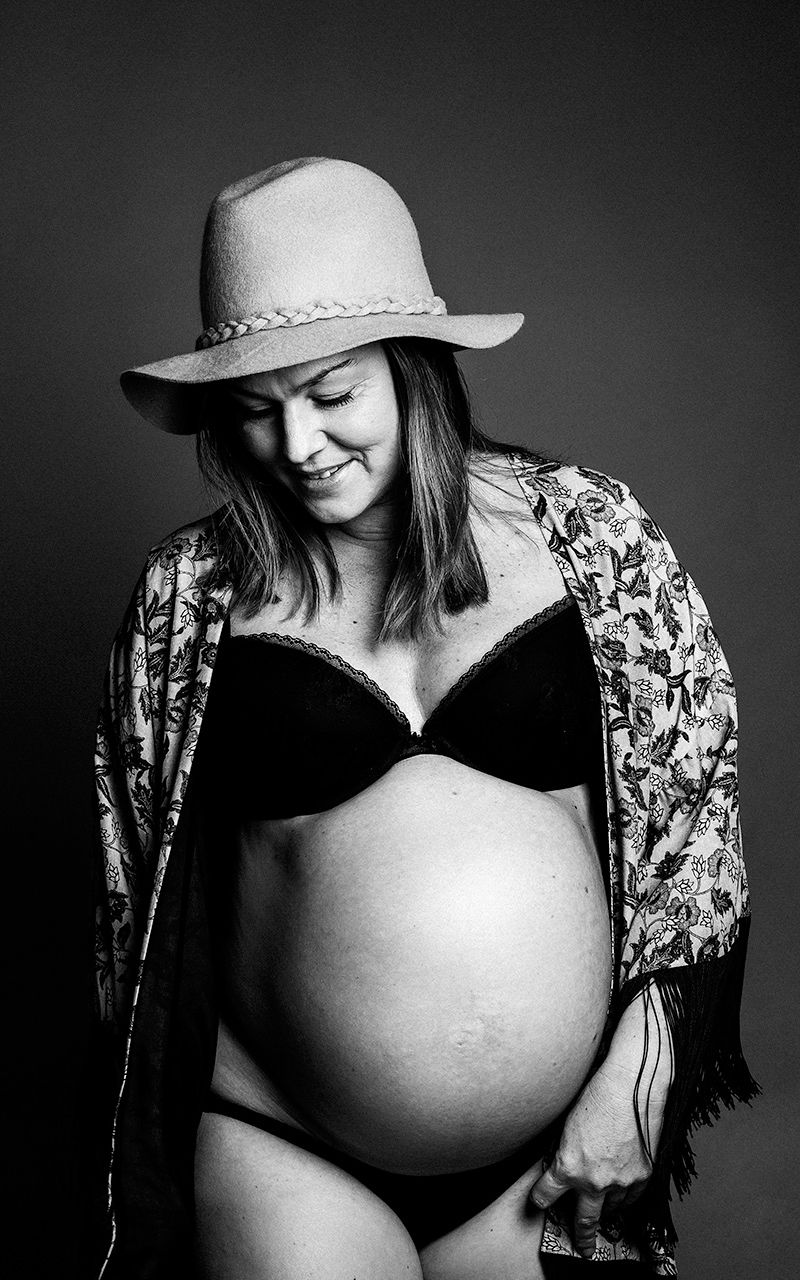 Schwangere Frau trägt einen Hut und lächelt im Fotostudio.