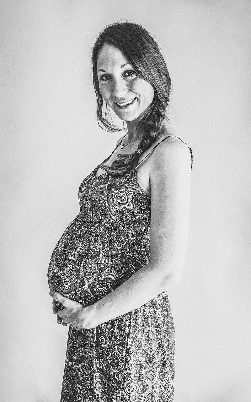Schwangere Frau steht im Studio mit Maxikleid.