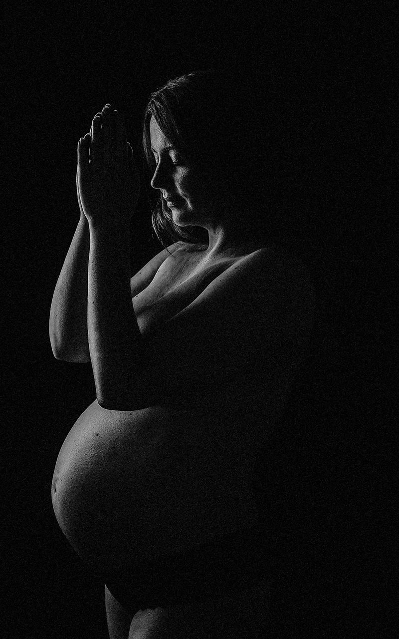 Silhouetten einer schwangeren Frau im Fotostudio vor schwarzem Hintergrund.
