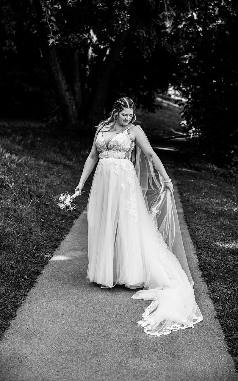 Braut steht im weissen Kleid auf Weg.