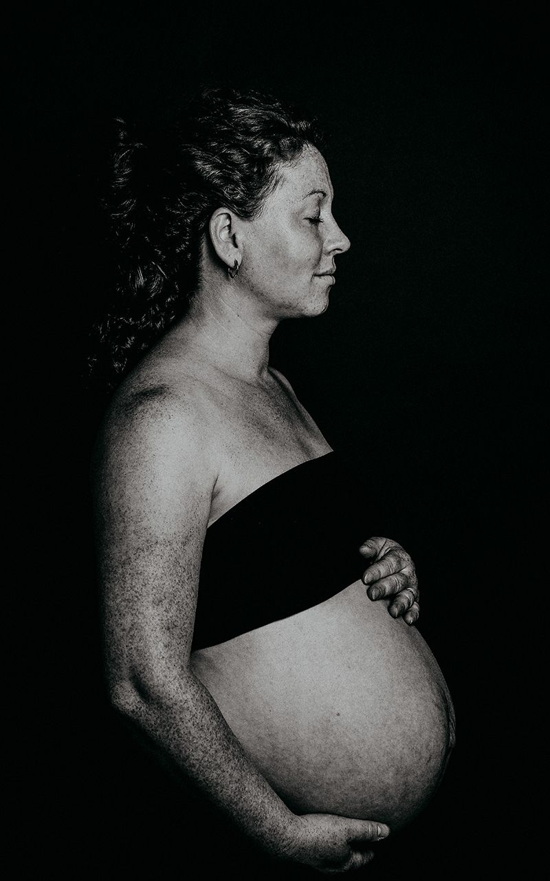 Schwangere Frau im Fotostudio mit schwarzem Hintergrund.