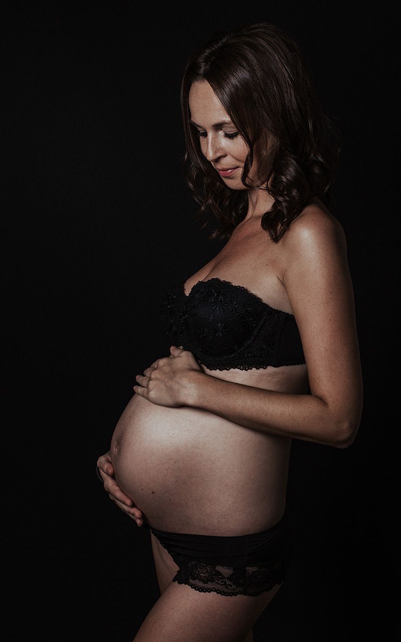 Schwangere Frau in schwarzer Unterwäsche die ihren Bauch hält.