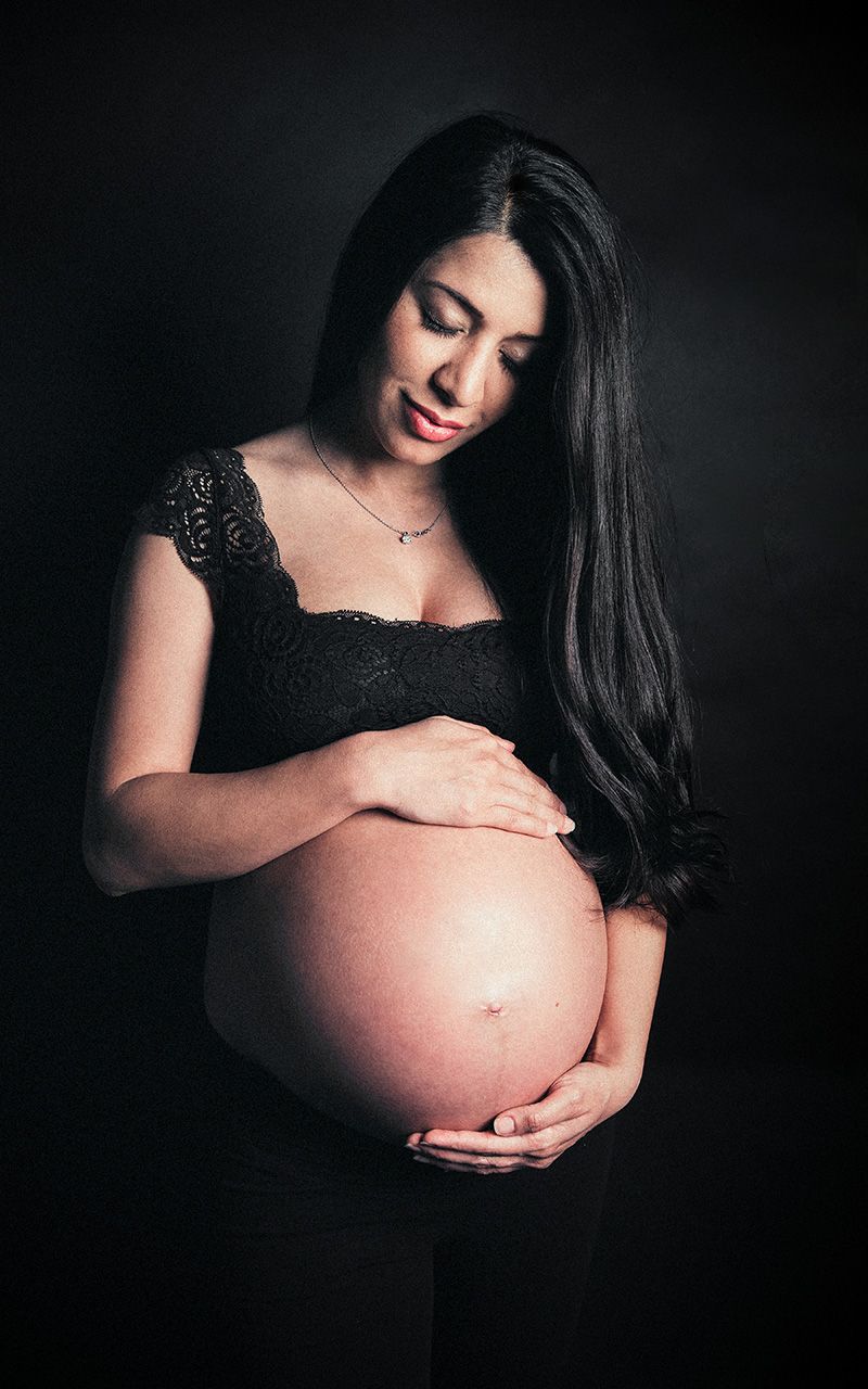 Schwangere Frau trägt schwarze spitzen Dessous und steht im Fotostudio.