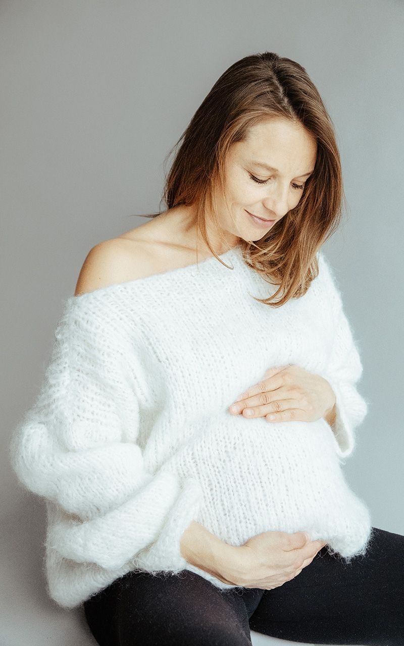 Sitzende schwangere Frau die ihren Babybauch ansieht.