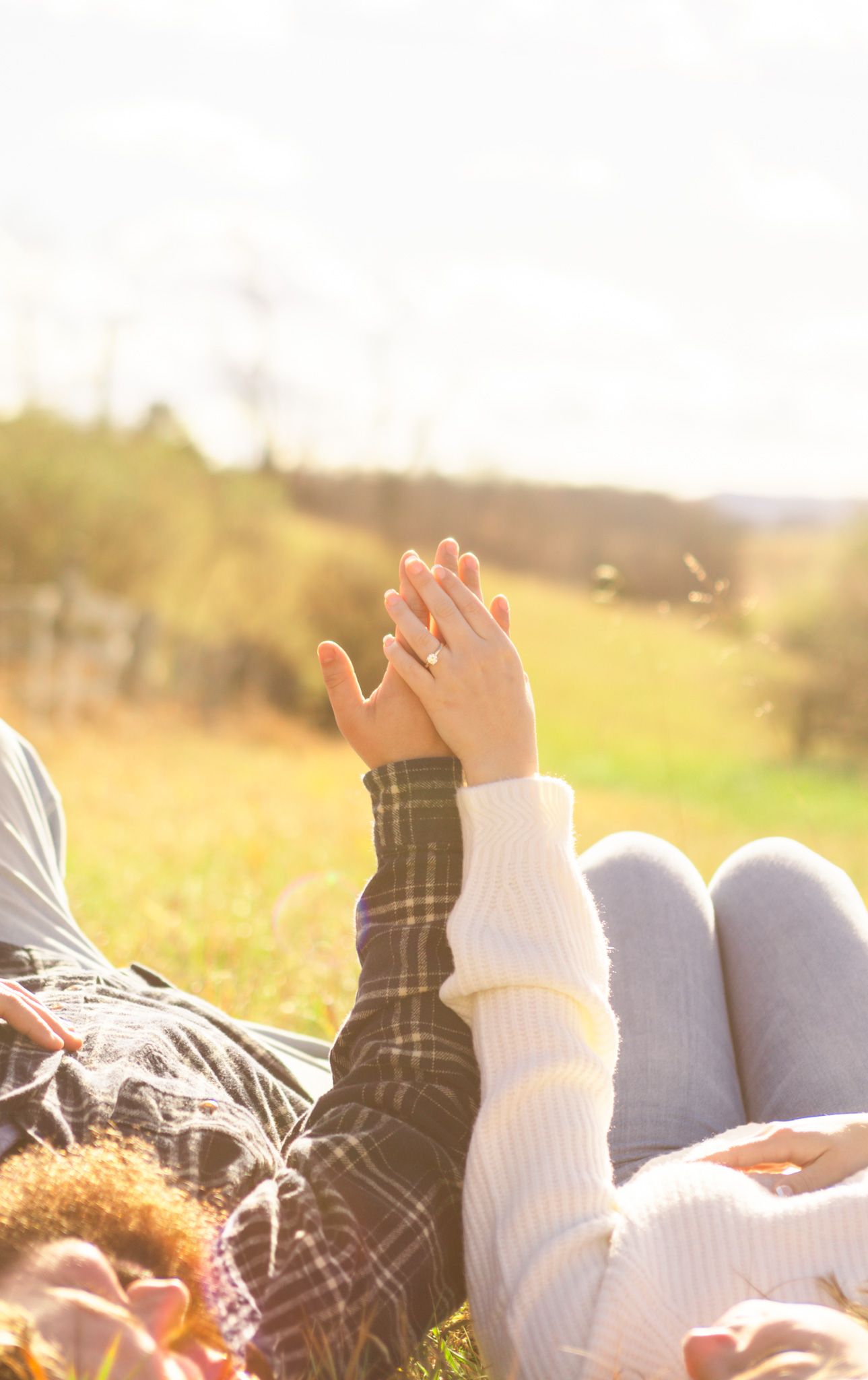 Couple holding hands while lying in a sunny green meadow during a golden afternoon.