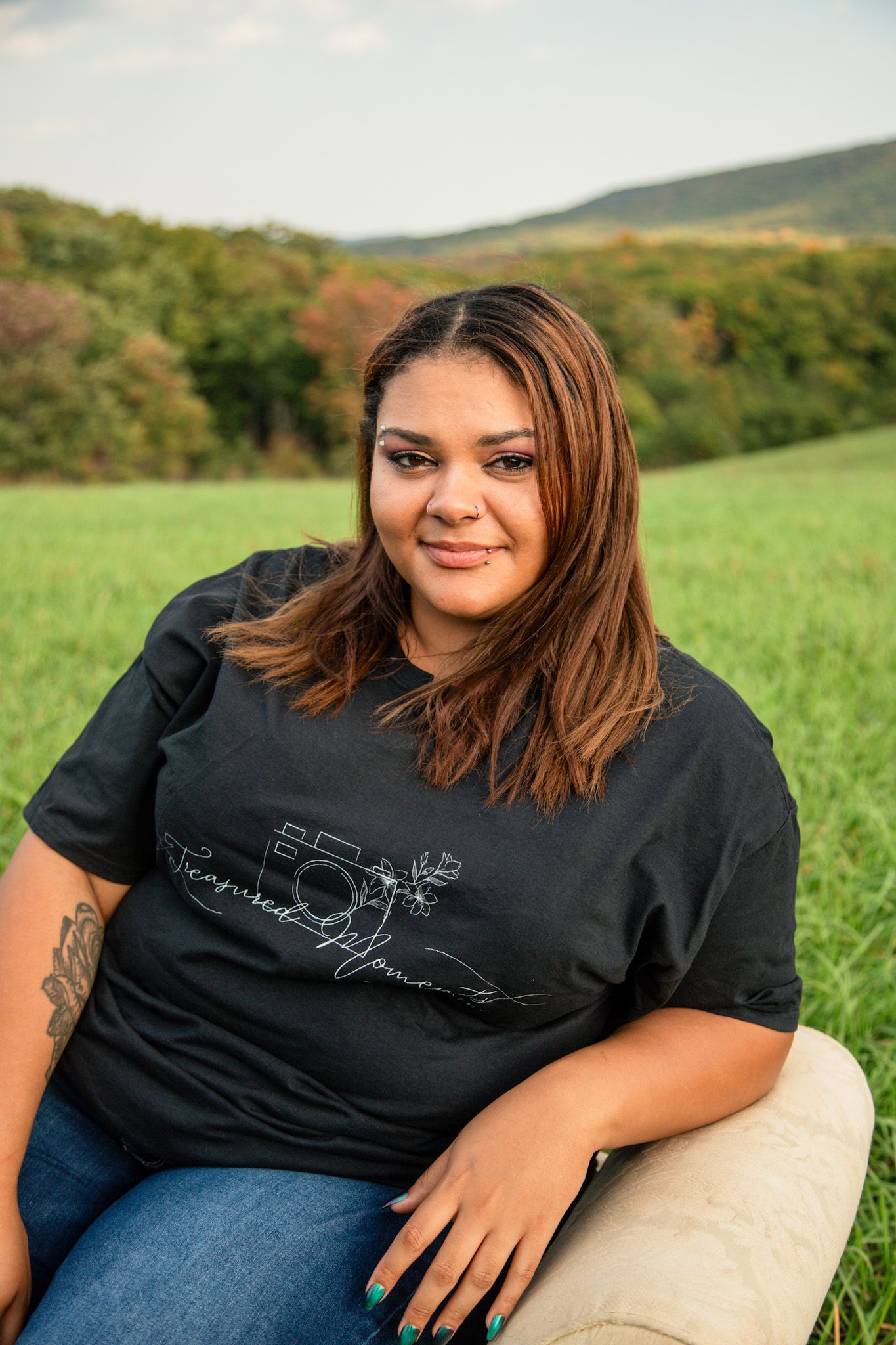 Woman in black graphic tee sitting in lush green field outdoors.