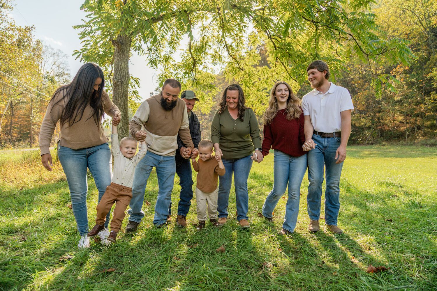 Happy extended family of seven walking and playing together in a sunny green autumn park.