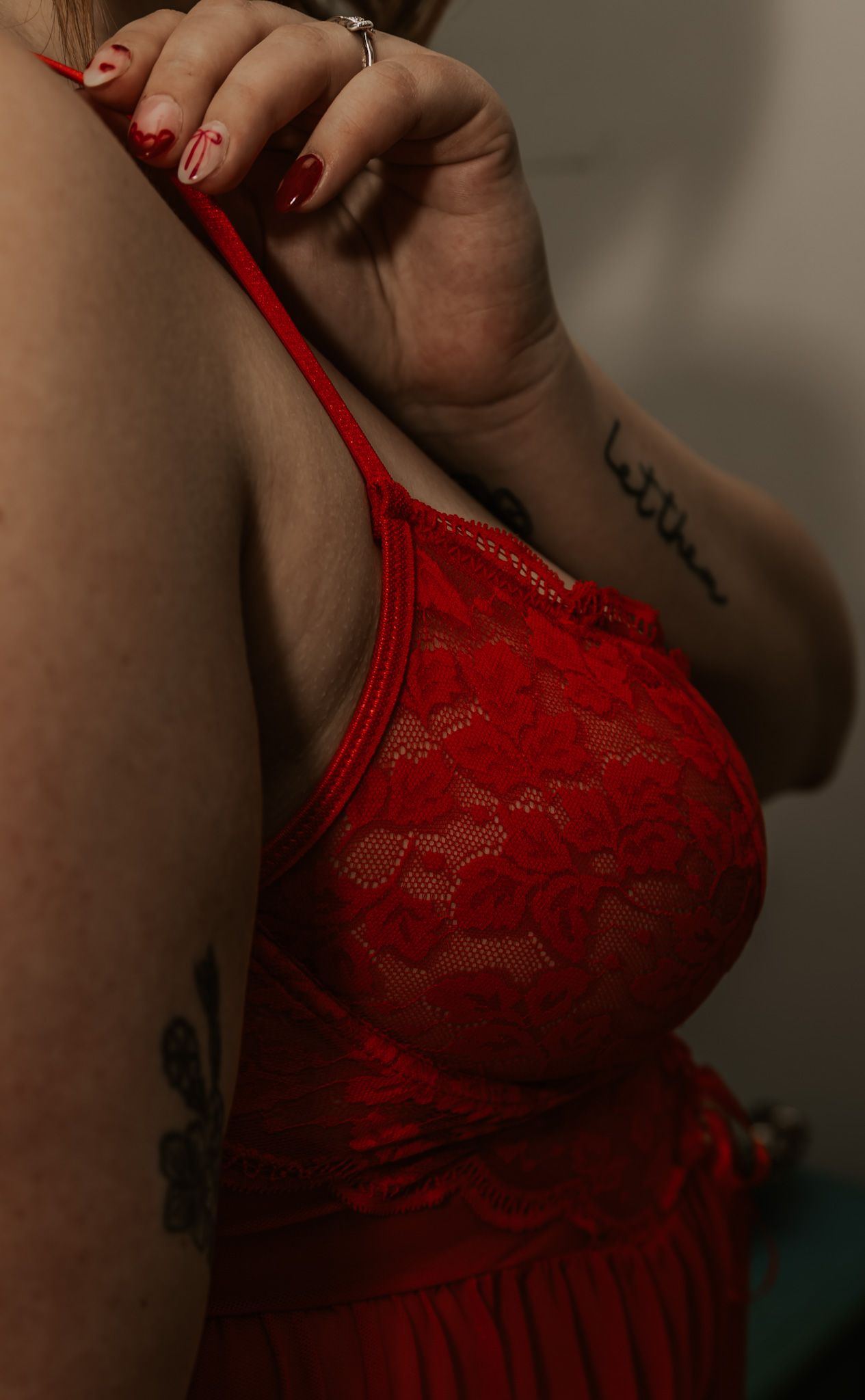 Close-up of woman in red lace lingerie with tattooed arm and red nails.