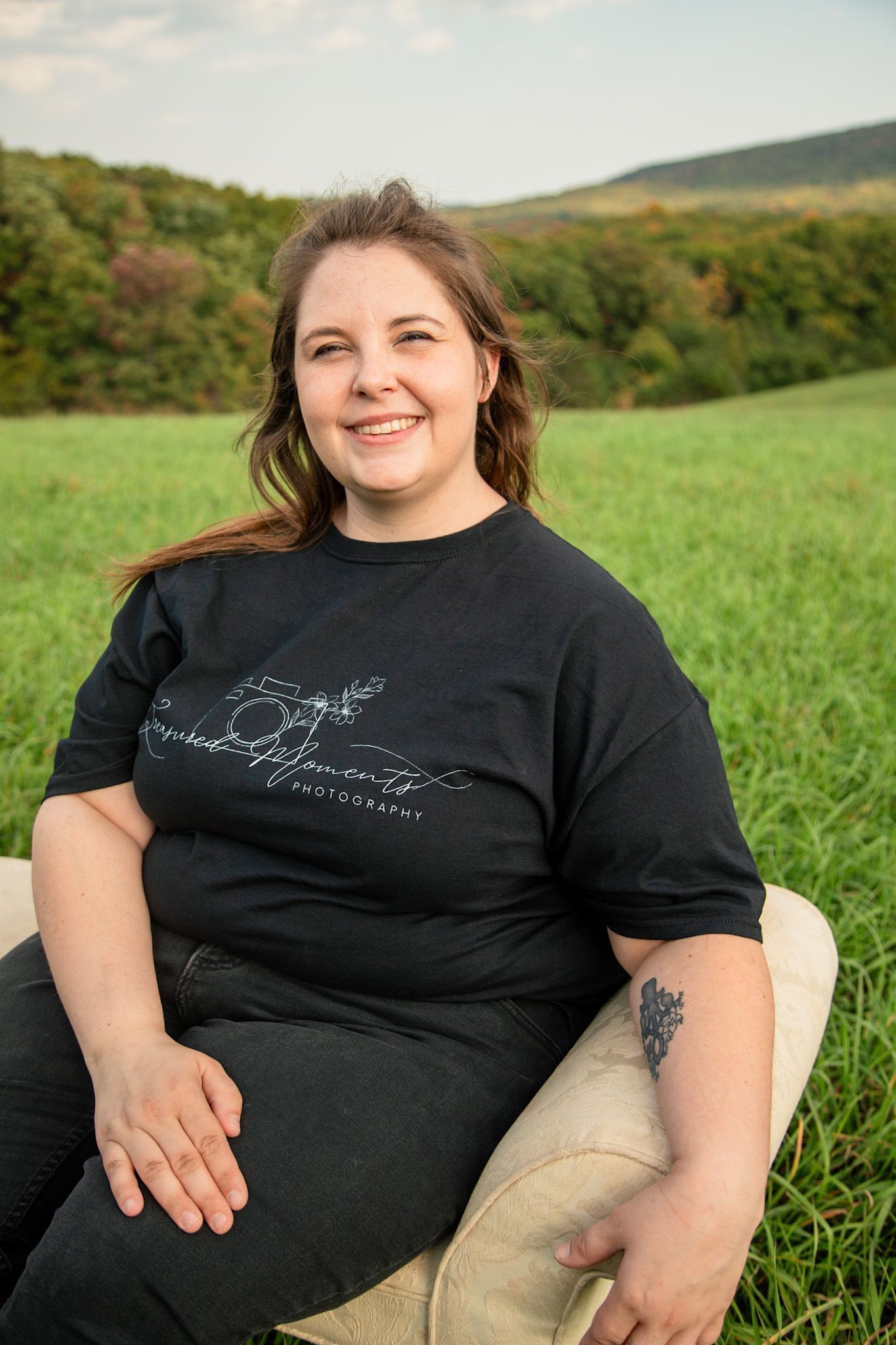 Smiling woman in black tee sitting in green meadow with hills.