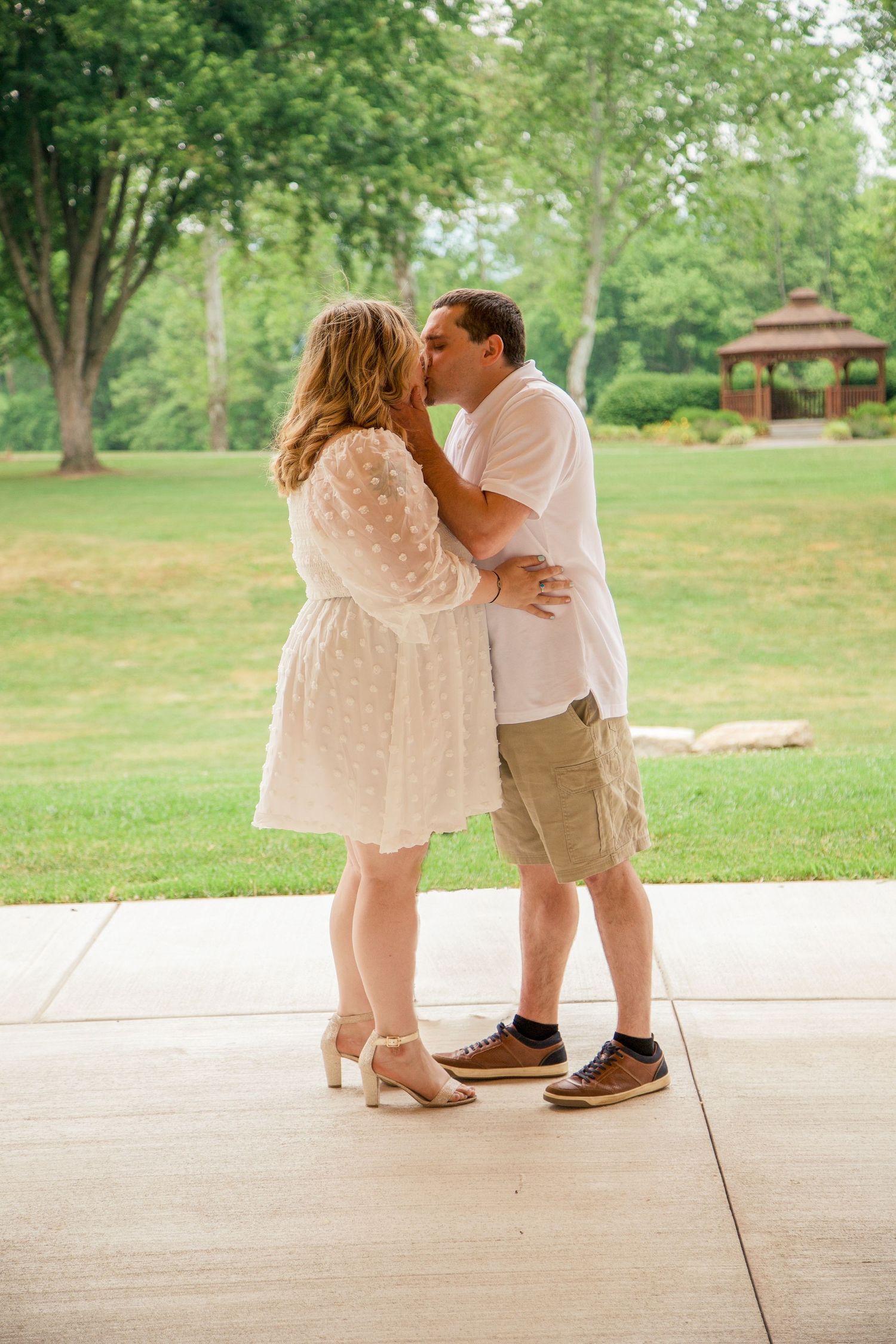 Couple sharing a kiss outdoors on patio surrounded by green park landscape.