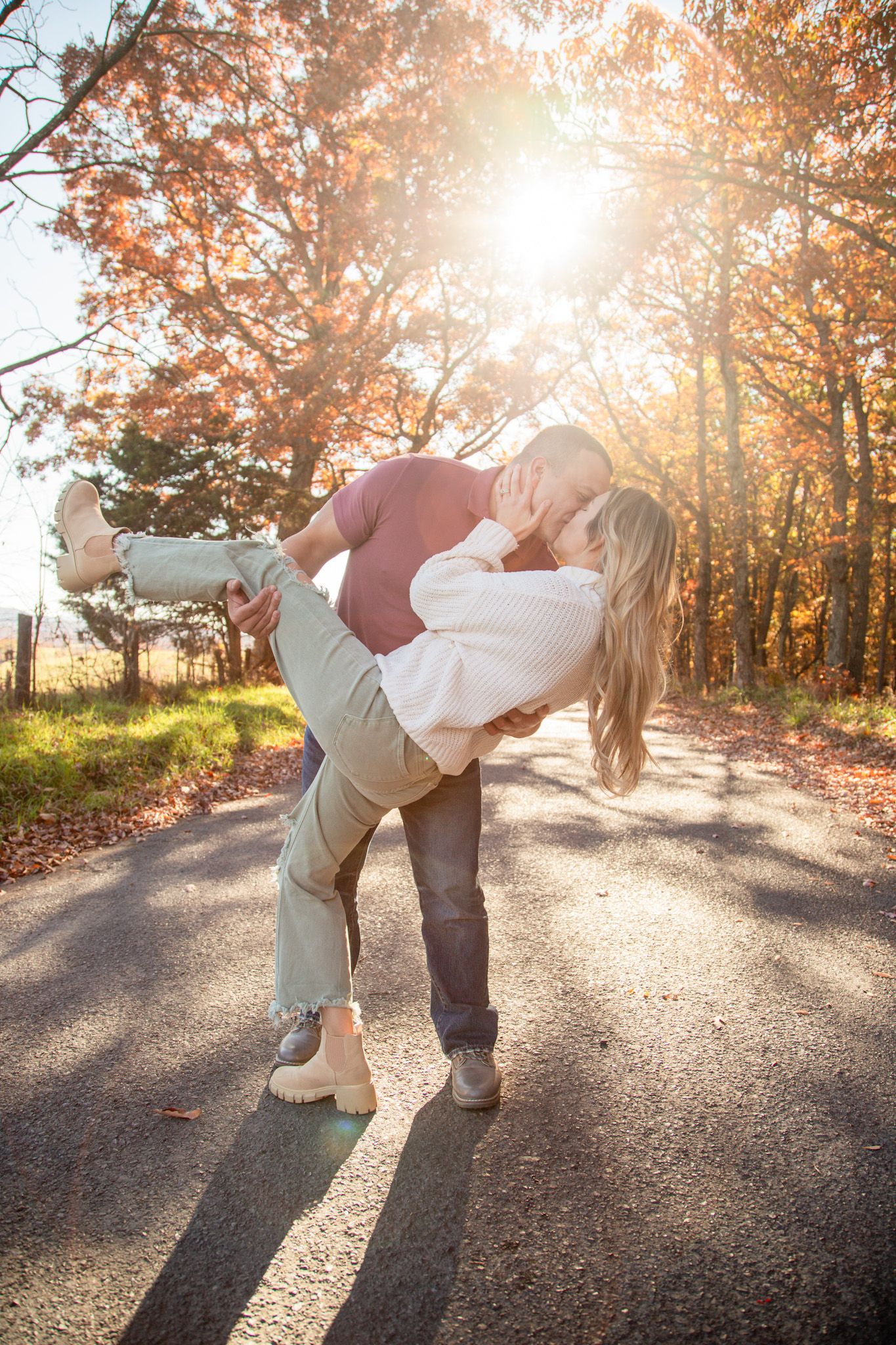 Couple sharing a romantic lift and kiss on a tree-lined road during golden autumn foliage season.