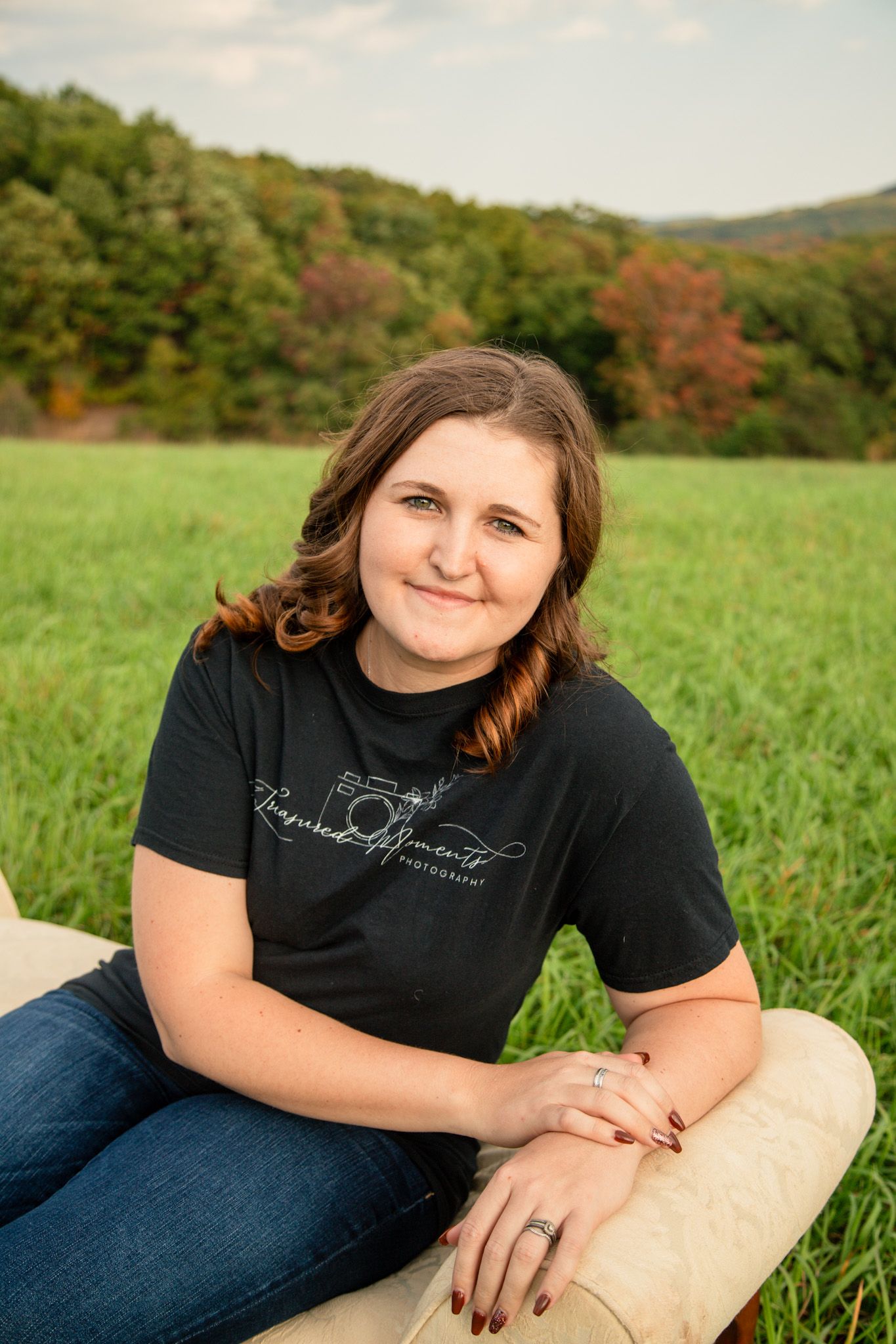 Smiling woman in black tee sitting in scenic green autumn field.