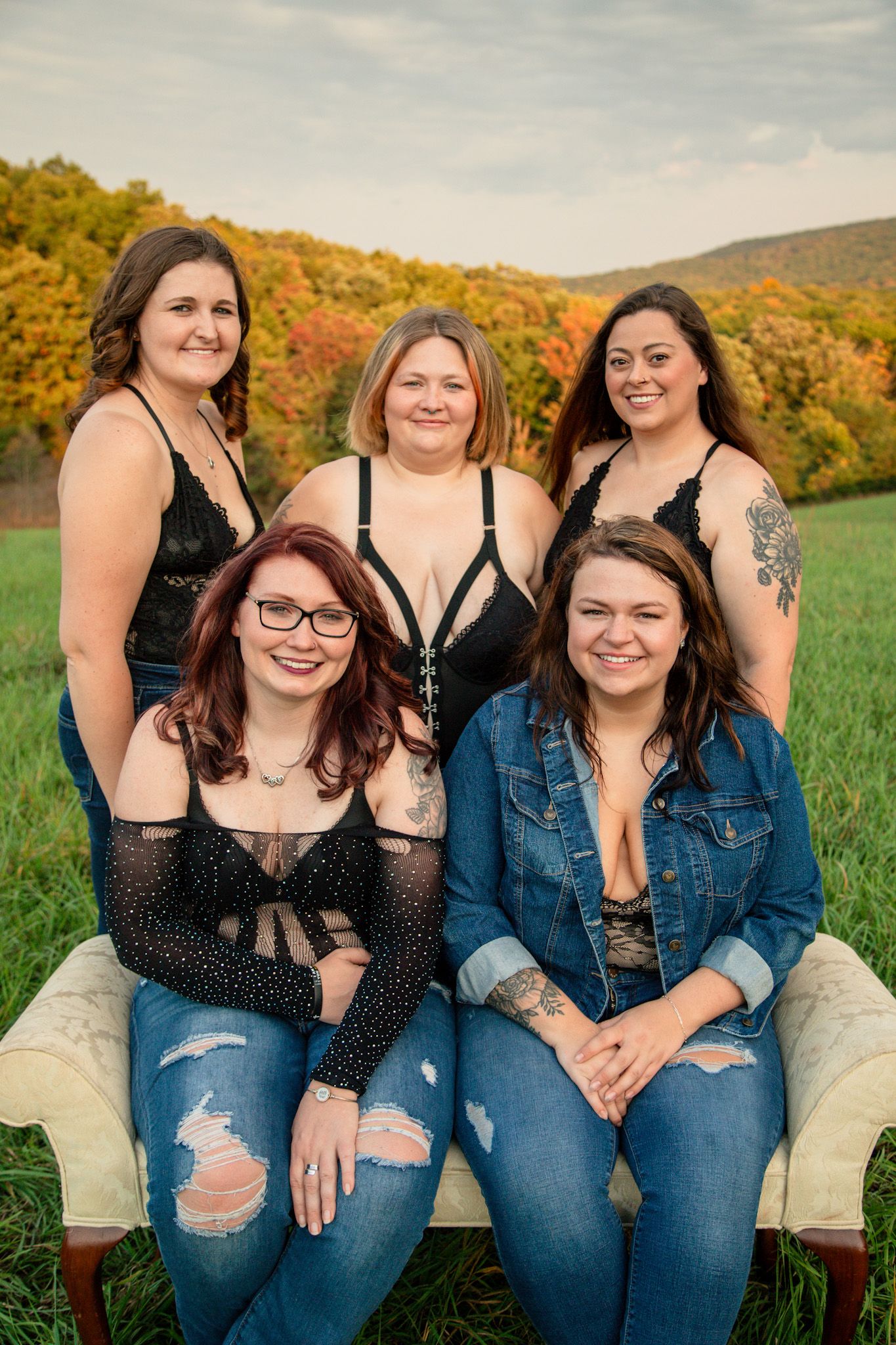 Five women in black lace and denim outfits posing on vintage sofa in autumn mountain field.
