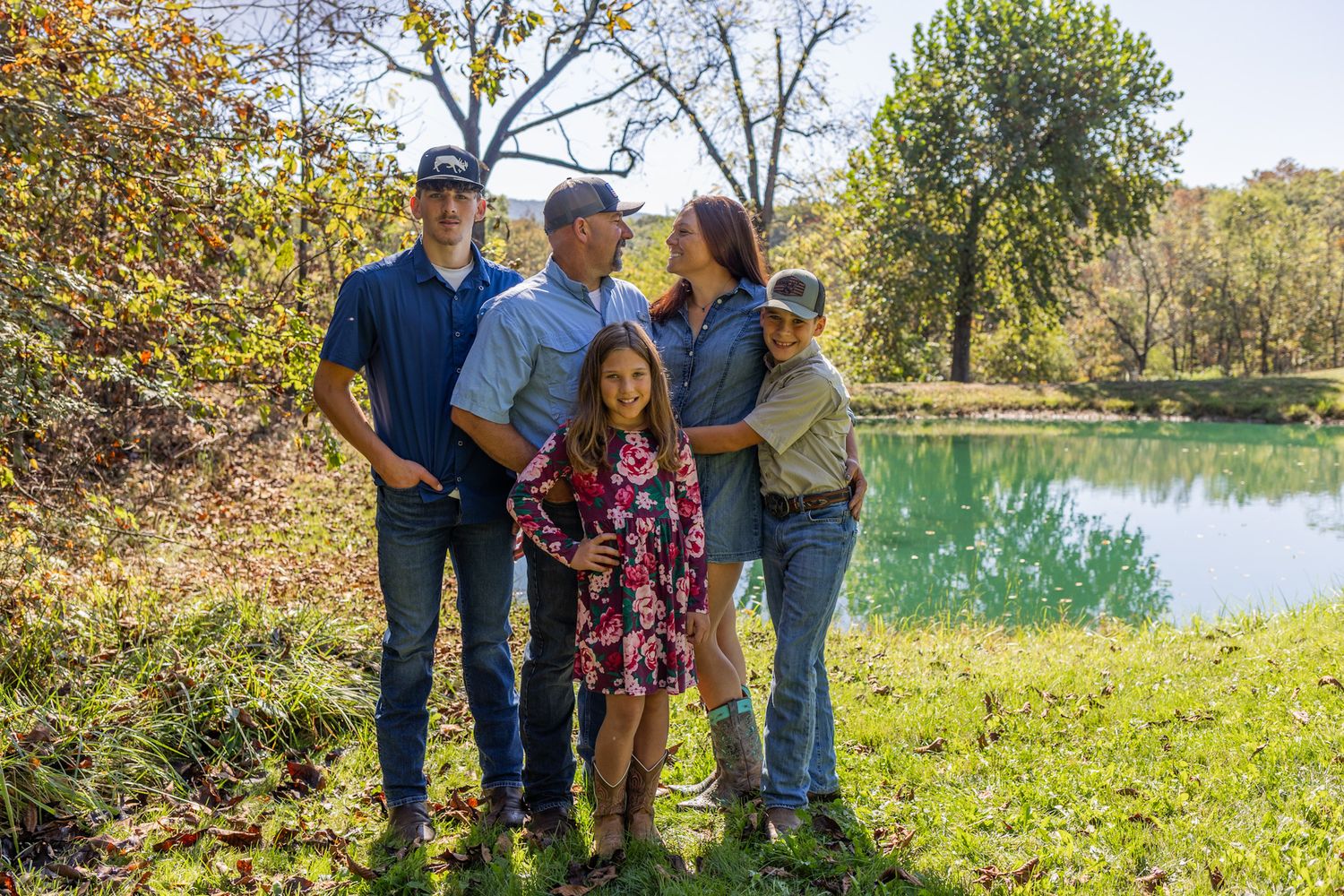 Happy family of five posing together near a reflective pond surrounded by colorful autumn foliage.