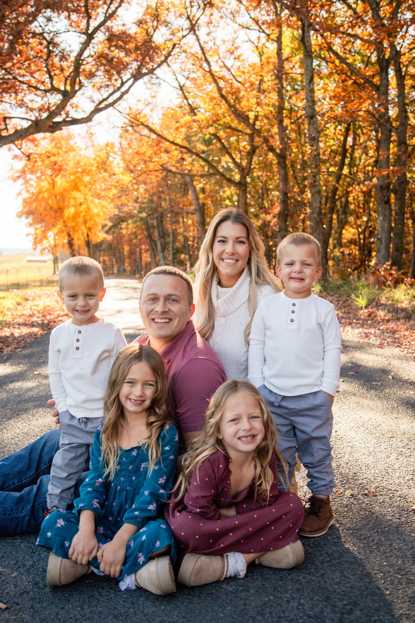 Happy family of six posing on a road surrounded by vibrant orange and red fall foliage trees.